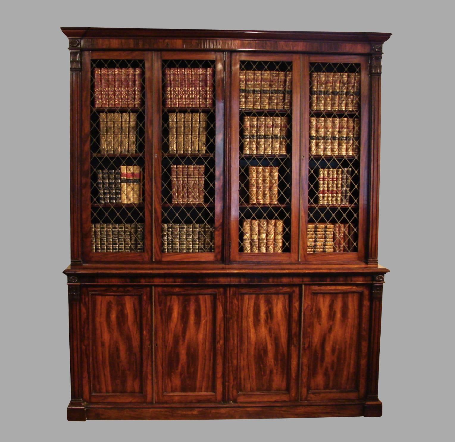 A lovely English Regency rosewood bookcase with columnar sides, the upper stage with four brass grille doors enclosing adjustable shelves above four cabinet doors with interior shelves, all resting on a plinth base. Lovely rich color. Interior is