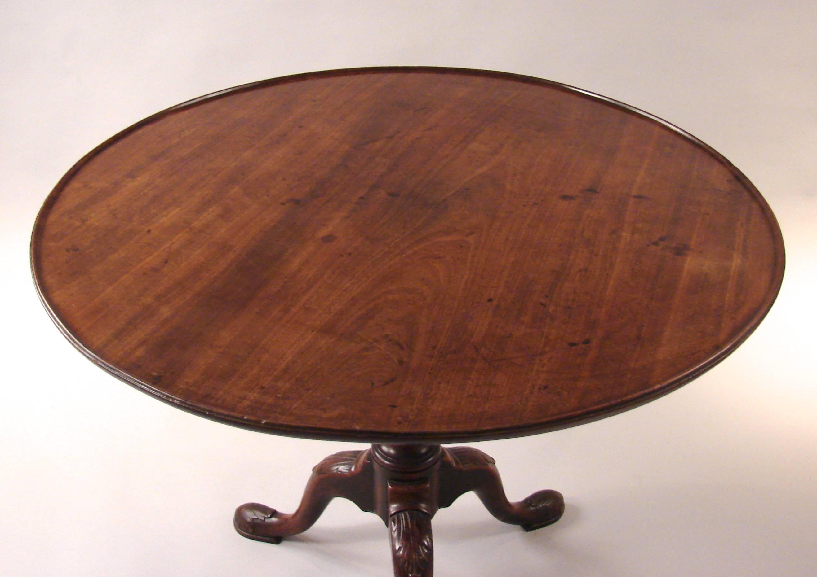 A George II mahogany tilt-top table, the large dish top above a carved standard ending in a tripod base with acanthus carved knees terminating in pad feet, circa 1760. This piece could be used as a breakfast table and can seat four people with ease.