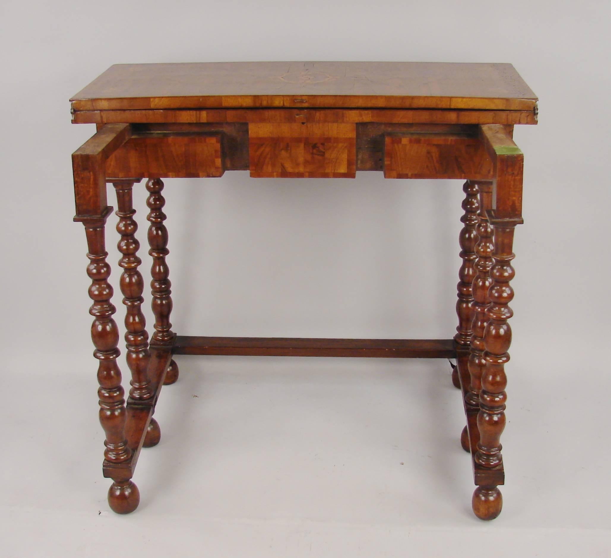 A William and Mary walnut marquetry inlaid gateleg game table with fold-over hinged top opening to reveal several compartments, raised on six ring-turned legs ending in ball feet and joined by flat stretchers, circa 1690.