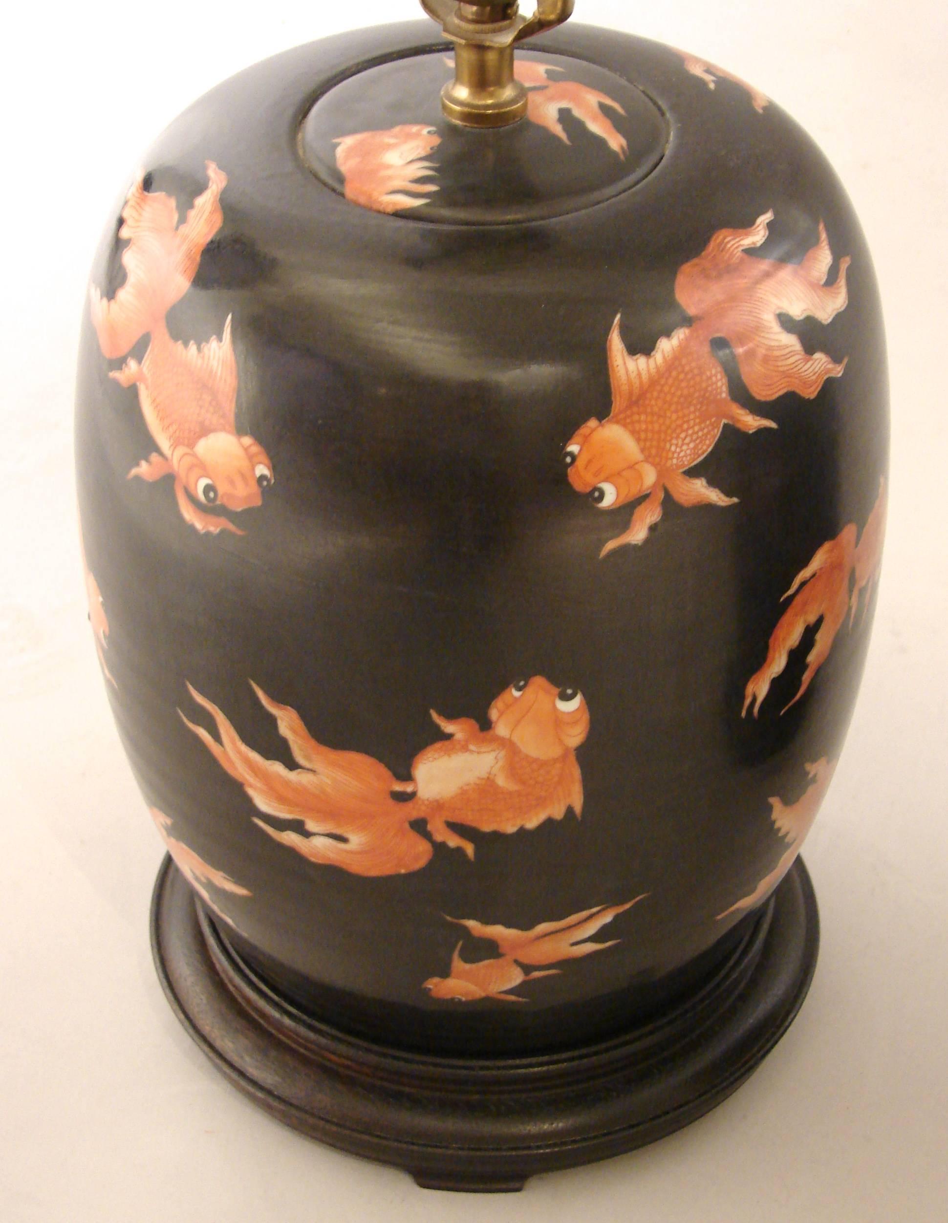 A decorative pair of black and orange goldfish decorated earthenware ginger jars with lids, now electrified and resting on carved wood bases. 20th century.