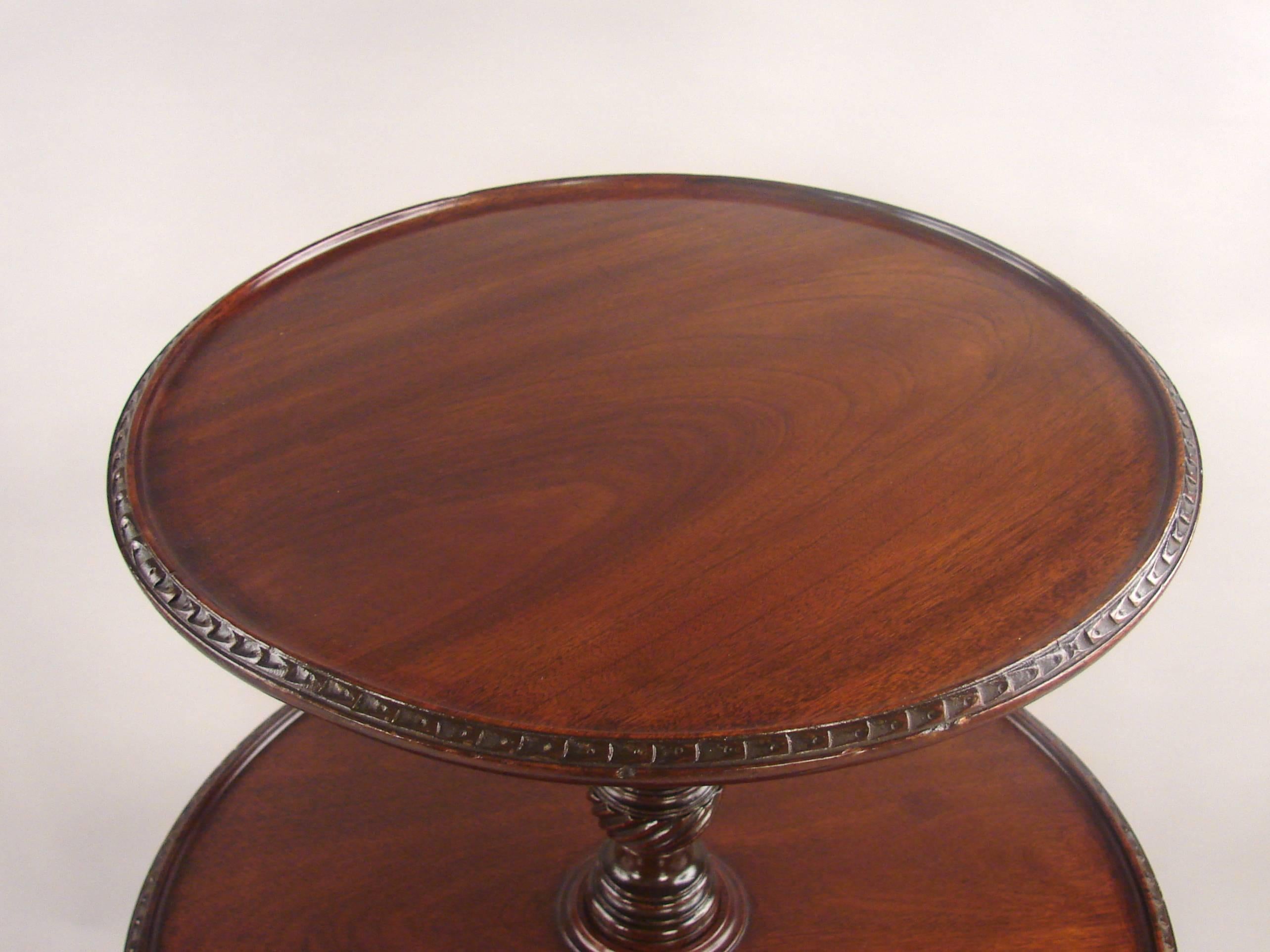 A fine George II mahogany three-tier dumbwaiter, each graduated shelf with a carved edge, joined by a carved and turned baluster standard, supported on a carved tripod base ending in pad feet on casters.