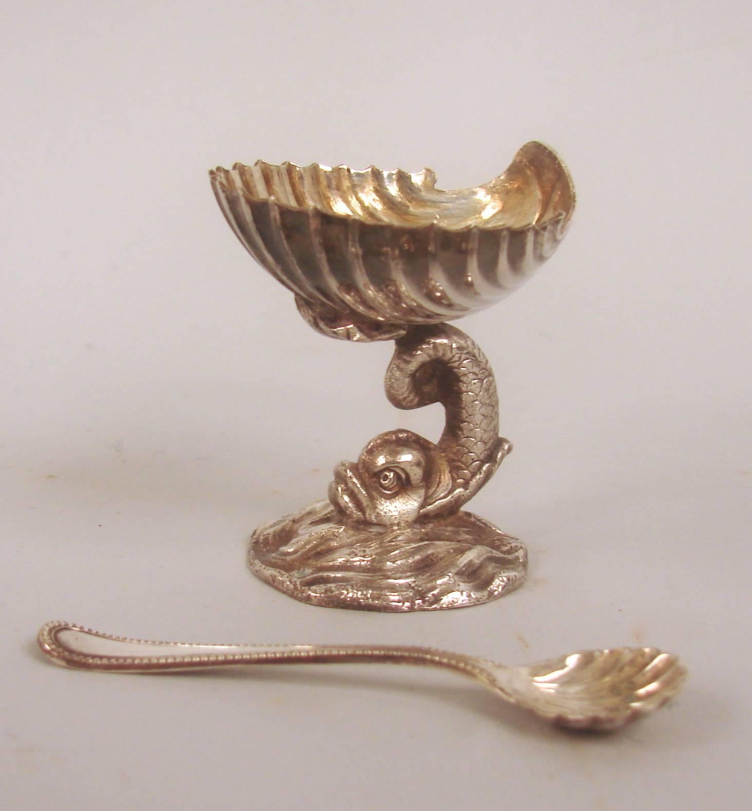 A cased set of six English silver plated salt cellars and spoons, each fashioned as a small compote with a shell form top on a cast dolphin form pedestal base, circa 1880-1900.