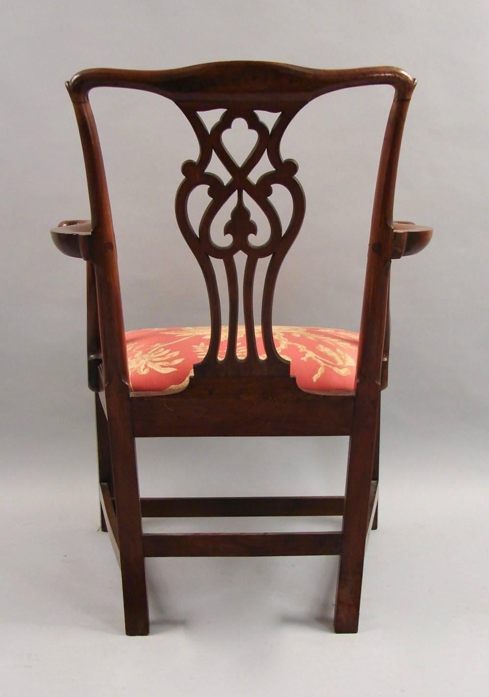 A good quality English mahogany Chippendale period armchair with a simple crest rail above an intricate splat, centered by elegantly fashioned arms, the rose brocade upholstery with a floral motif, all supported on straight legs joined by