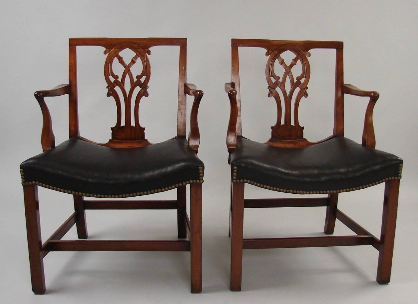 A fine and unusual set of 4 Georgian leather upholstered mahogany armchairs with nailhead trim, the square crest rail over an elaborate carved splat, the shaped arms terminating in a saddle seat, all supported on square legs joined by a box