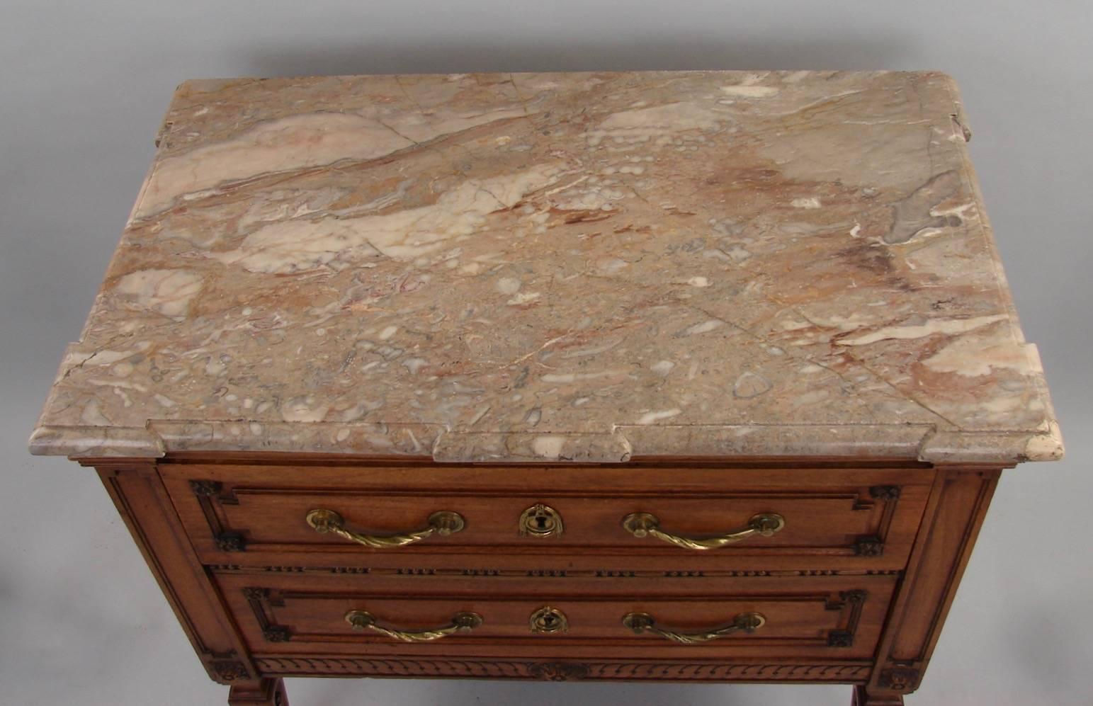 A good continental neoclassical walnut two-drawer commode, the variegated cream colored marble-top above a molded edge over two inset paneled drawers decorated with bosses, the sides similarly treated, all supported on carved tapering legs. Stamped