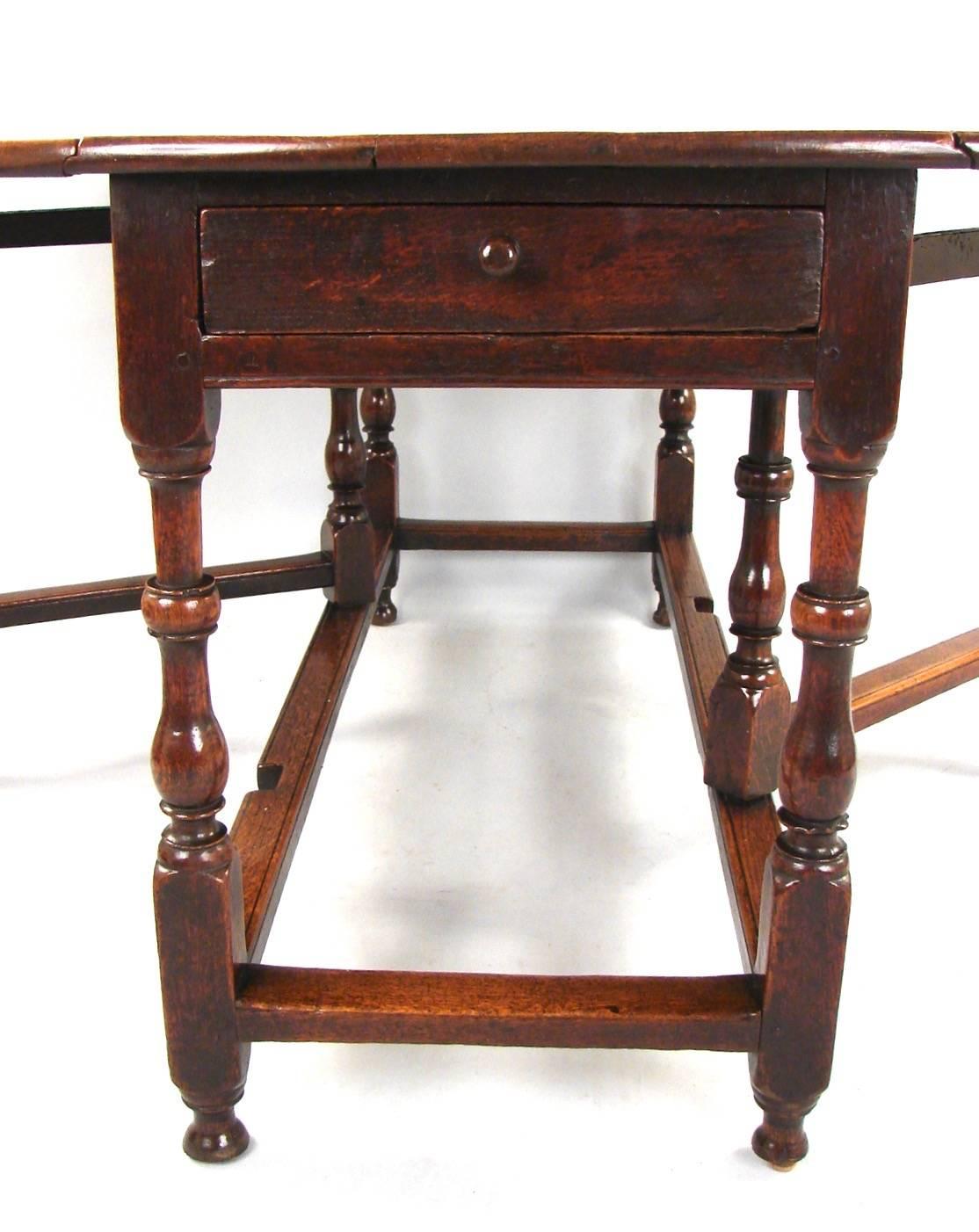 A substantial English oak drop-leaf table, the patinated light oak top above a single drawer supported on well-turned legs ending in shaped feet, circa 1690-1700.