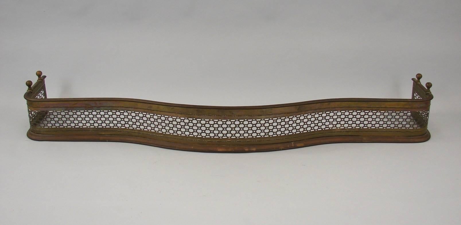 An English brass fireplace set consisting of a large serpentine grillwork fender, three tools and a pair of firedogs.