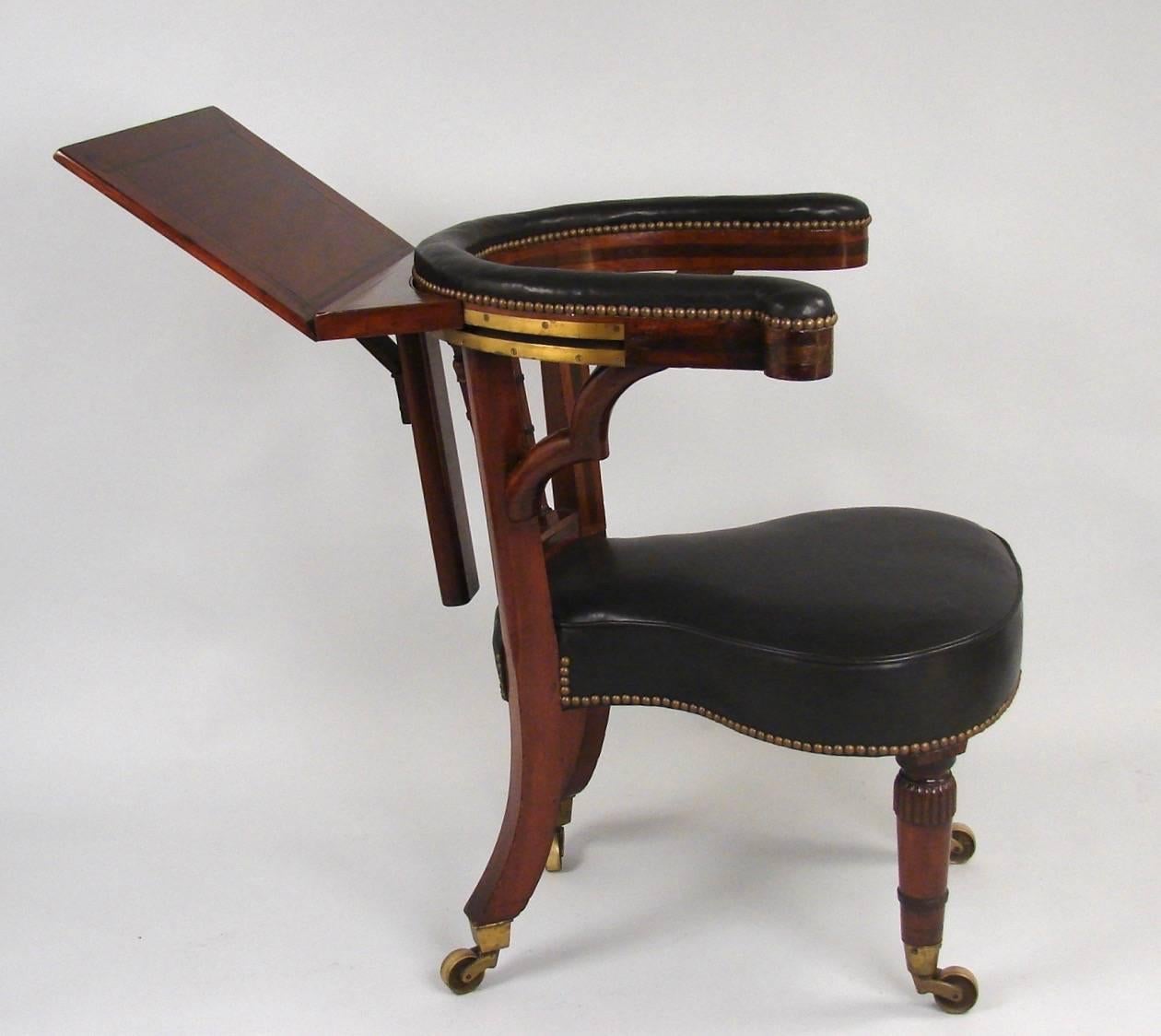 A Regency period mahogany part-ebonized leather upholstered library reading chair, the U-shaped top rail with a sliding ratcheted reading panel on the back above an upholstered seat raised on tassel carved and ring turned tapering legs ending in