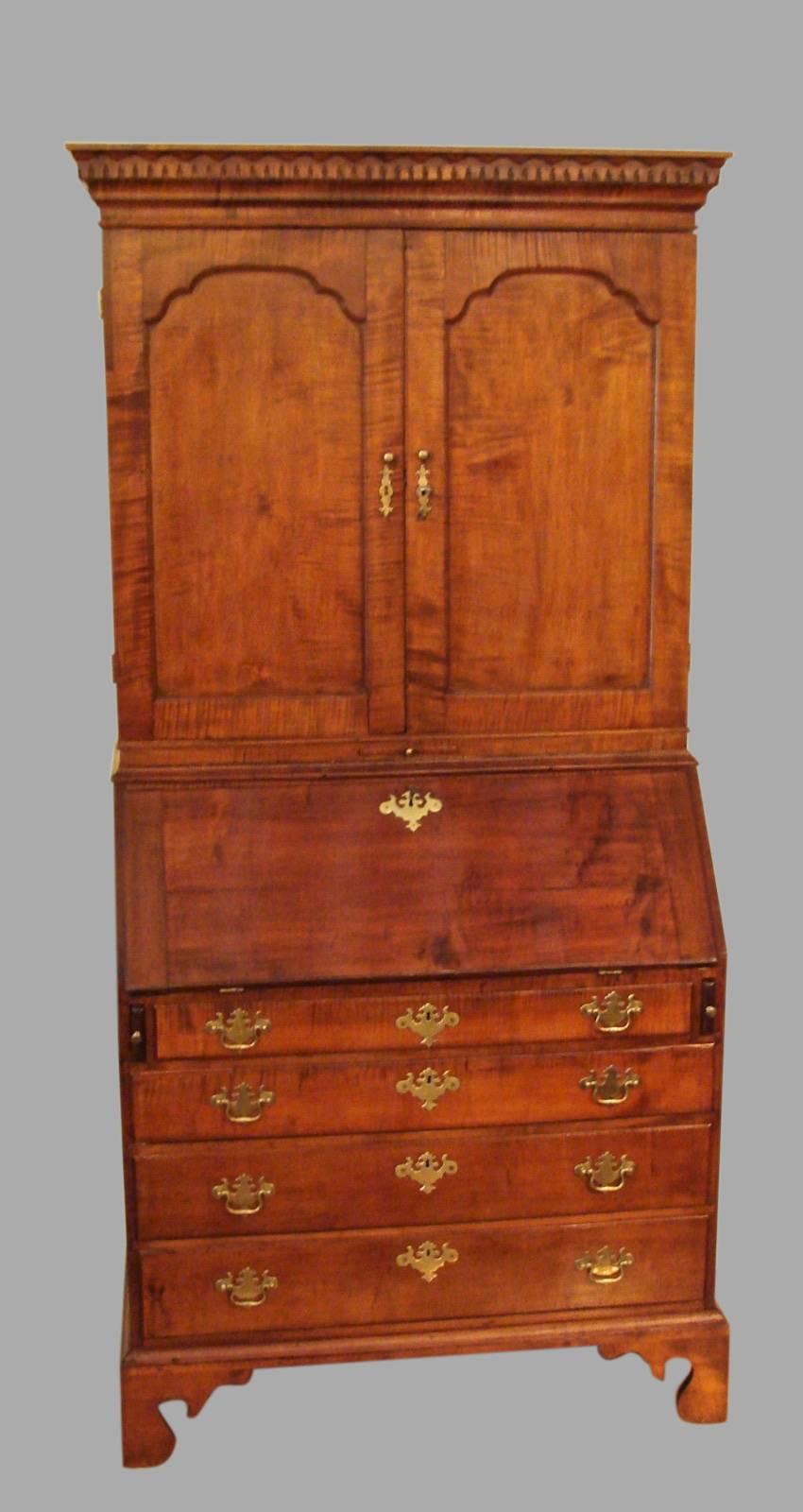 An American (New England) tiger maple secretary bookcase, the paneled cupboard doors concealing eight compartments above four small drawers, above a fall front desk with a well-fitted interior over four graduated long drawers supported on bracket