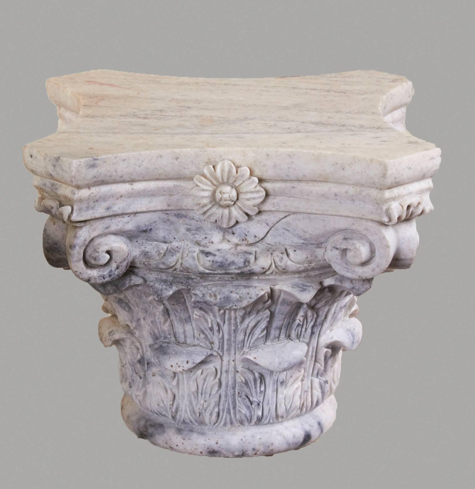 A pair of Italian Carrara marble Corinthian capitals of typical form with floral and scroll decoration. Weathered patination. Probably 20th century. Heavy.
