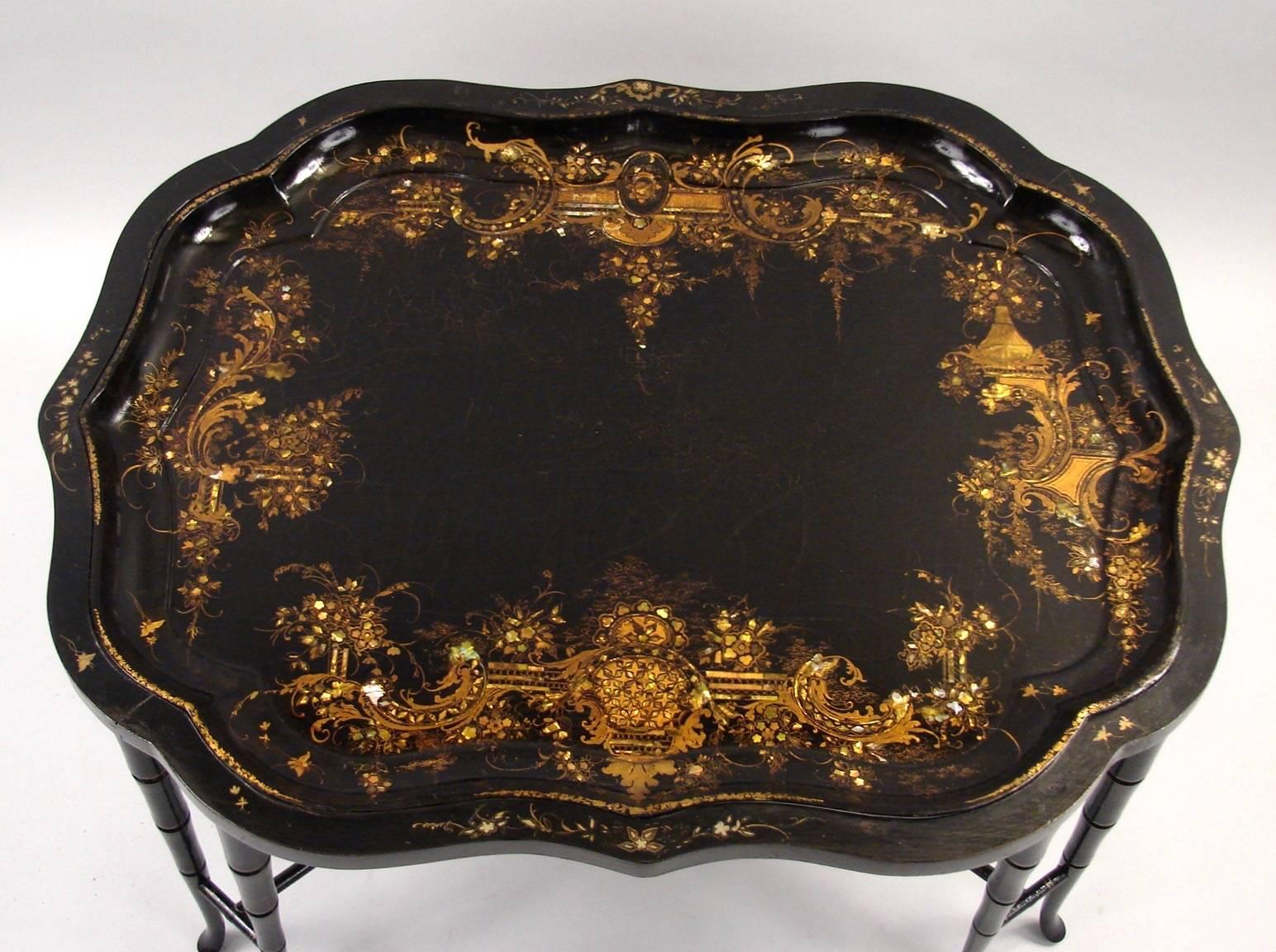 A good quality signed papier mâché scalloped edge tray with elaborate mother-of-pearl gilt heightened inlay signed on the back Jennens and Bettridge makers to the Queen now mounted on a decorated faux bamboo eight legged stand of a later date. The