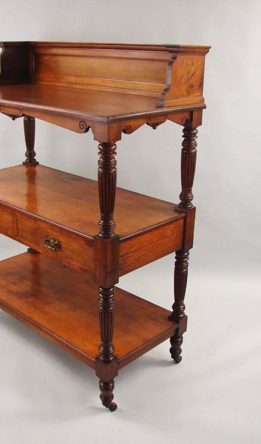 A good quality English Victorian period walnut three-tier server of architectural form, the galleried top above three shelves and two central drawers flanked by fluted columns, resting on turned feet, with brass casters. Labeled on the back S.G.