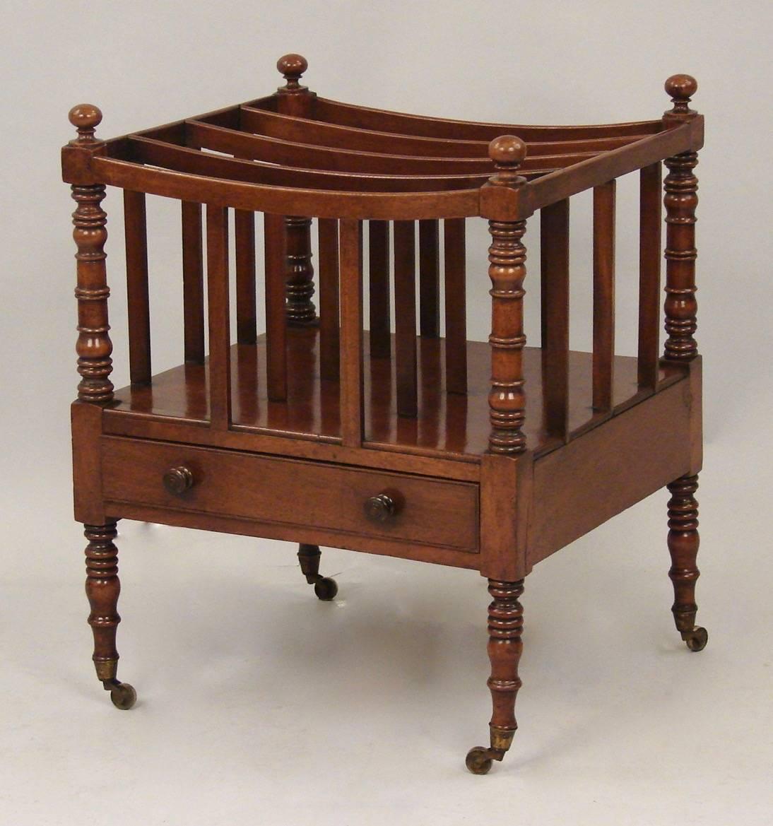 A Regency mahogany four section canterbury with a single drawer, the body with well-turned corner supports, the legs similarly structured and ending in original brass caps and casters, circa 1825-1830.