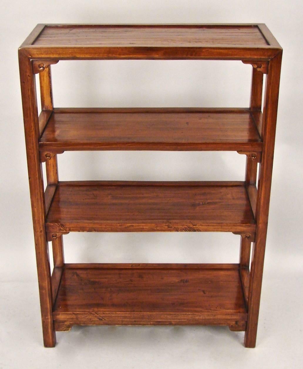 An attractive and useful small-scale Chinese bookcase, the inset top above three additional shelves, each with a stylized bracket, the shelves made of well-figured elm with a polished surface supported on straight legs, circa 1900-1920.