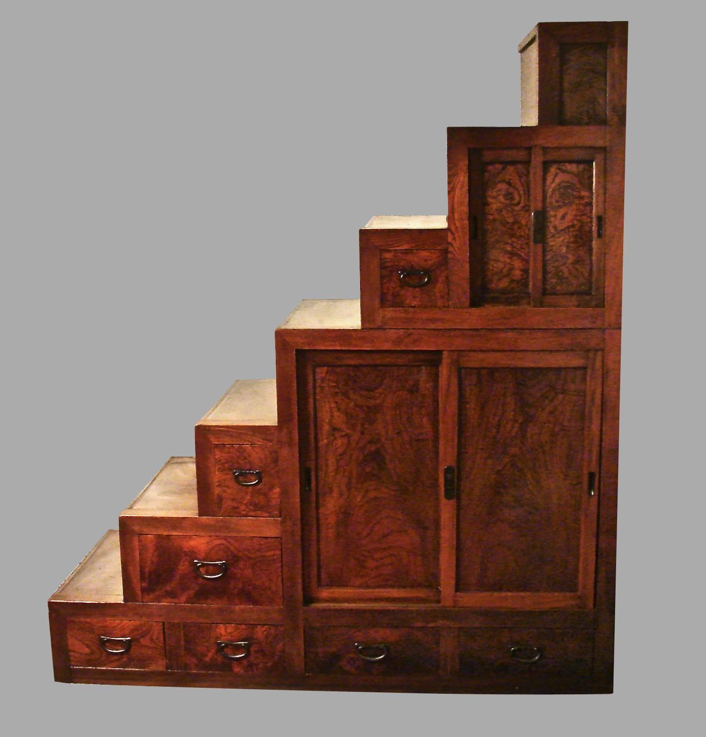 A good quality late Meiji period Japanese keyaki wood kaidan or step tansu in two parts, the small three step upper stage with two sliding doors and a single small drawer, the large lower stage with four steps, two sliding doors and six drawers of
