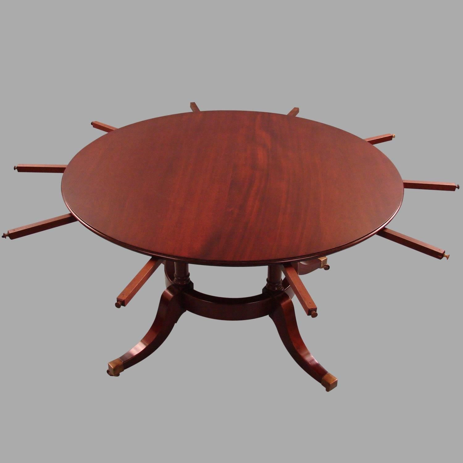 A Regency style circular mahogany dining table with five outer extension leaves, supported on a quadripartite base joined by a circular element, the down swept legs resting on brass caps and casters, 20th century.