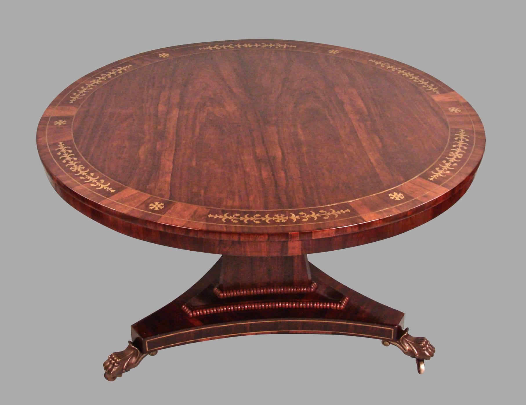 A fine quality Regency rosewood center table, the top with a lovely inlaid brass floral design, the base with a stepped beaded platform further inlaid with brass, all supported on cast bronze animal paw feet ending in casters, circa 1815.