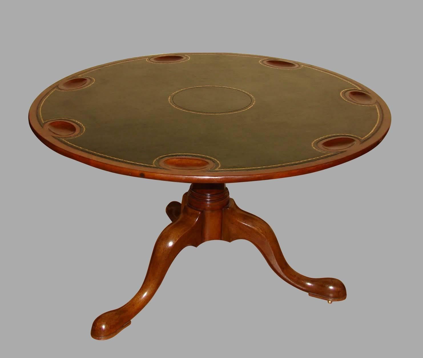 A round George III period mahogany tilt-top games table, the gilt-tooled green leather top with seven wells, supported on a turned central column with three cabriole legs terminating in pad feet on casters, circa 1770.