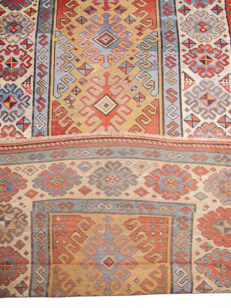 Woven in the southeastern Transcaucasus region in what is now the Republic of Azerbaijan, this happy rug experiments with two variations on a theme. Against a camel field, a column of diamond latch hook ornament is drawn and flanked on either side