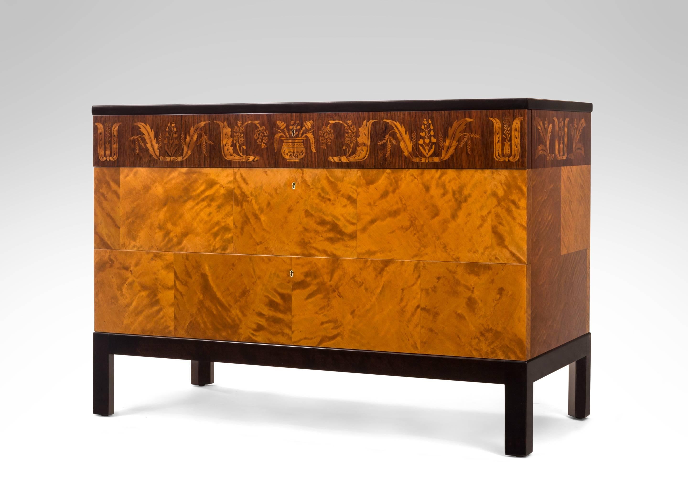 The rectangular figured birch top, above an inlaid rosewood frieze drawer and two figured birch drawers, on an ebonized base with square legs.