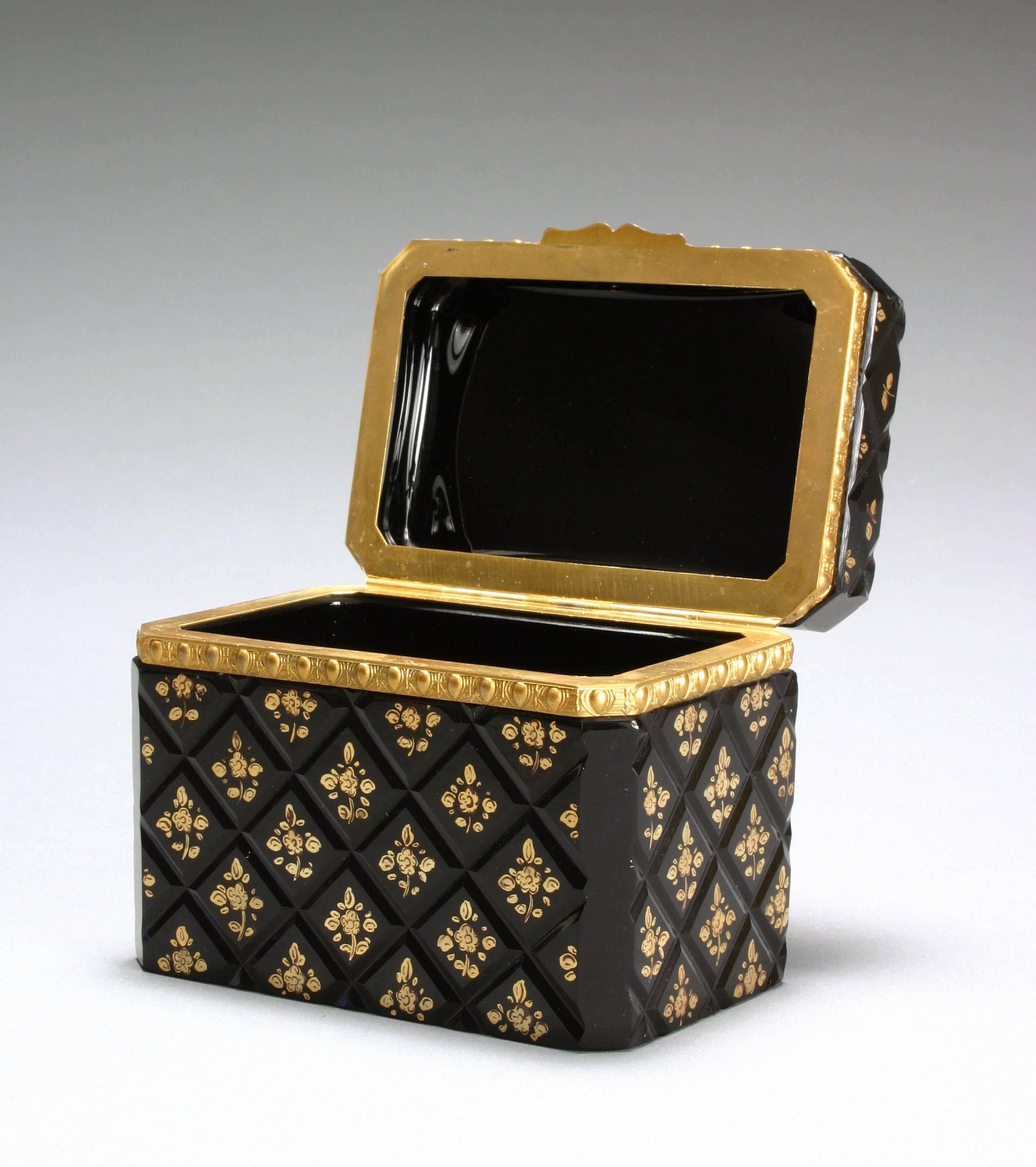 The rectangular cover with canted corners on a conforming base banded with an egg and dart frieze and scroll clasp, the glass surface cut in a diamond pattern grid with each square centered by a gilt nosegay. 