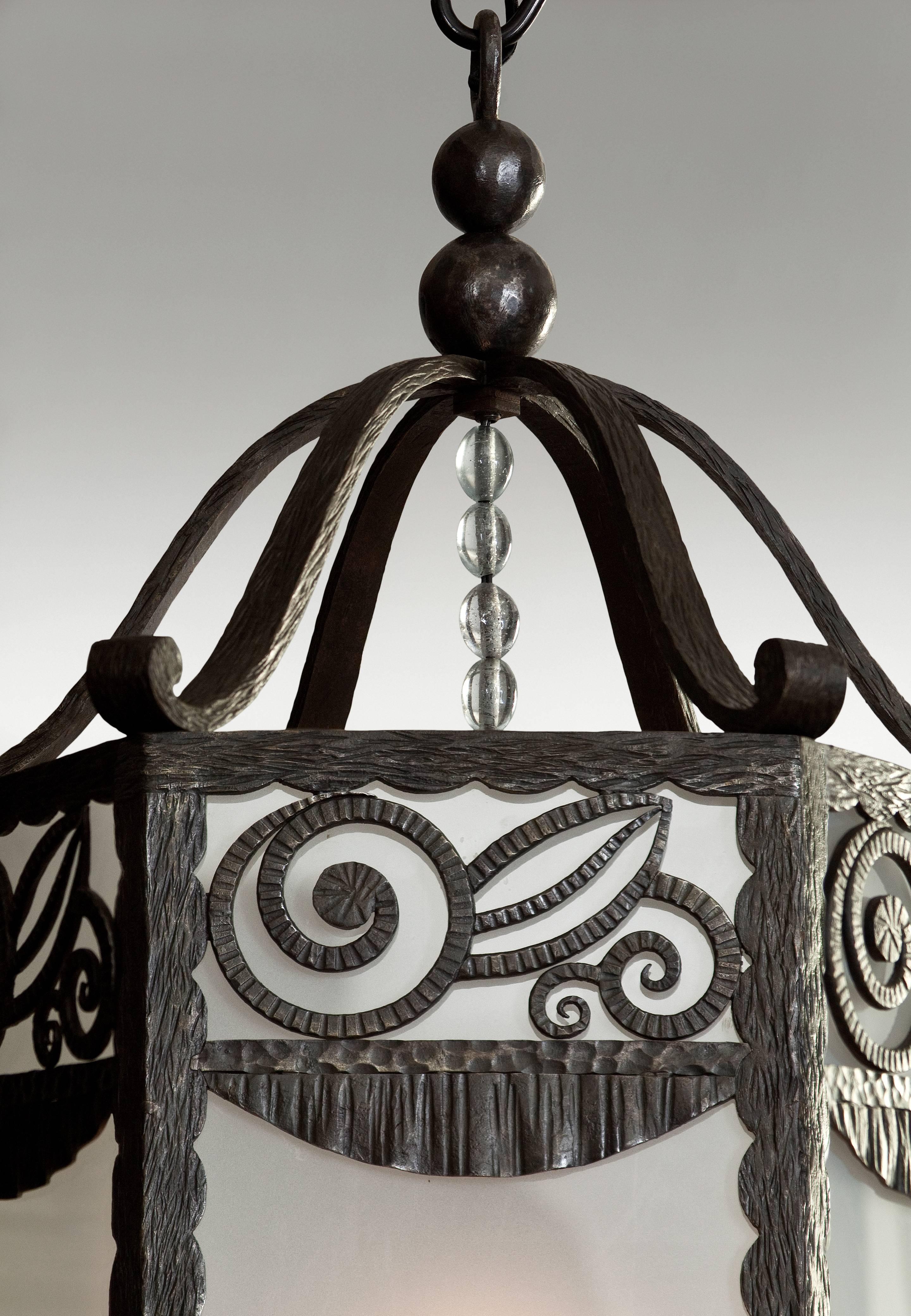 The lantern surmounted by two spheres issuing s-scrolls, above a floral frieze and rectangular panels silhouetted by opaque glass, the light fixture suspended by rock crystal beads, terminating in iron tassels.