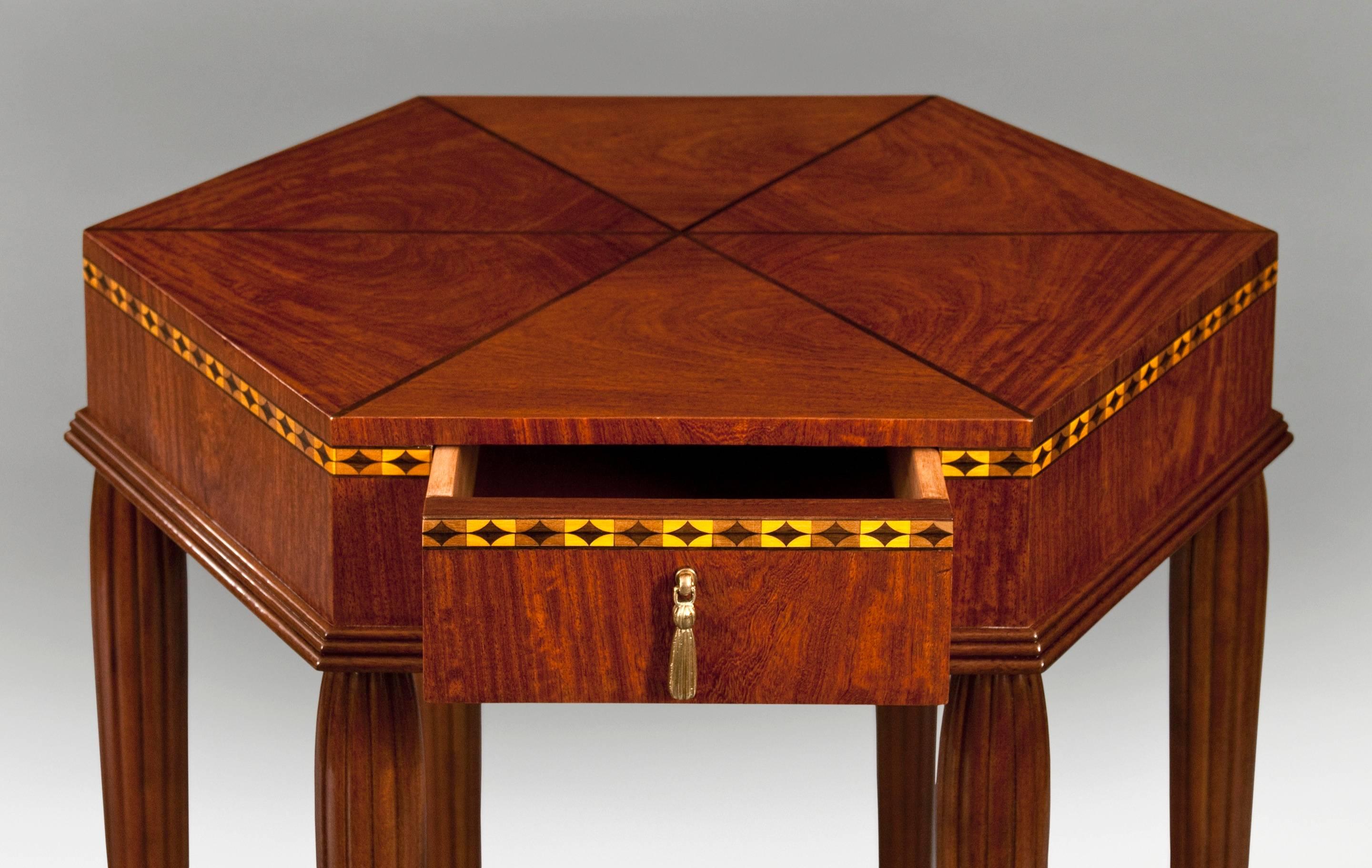 French Art Deco Ash and Bubinga Hexagonal Table With Drawer
The hexagonal top with radiating ebonized banding, above a conforming apron with diamond parquetry and a molded base, centering a single drawer with bronze tassel pull, on six fluted