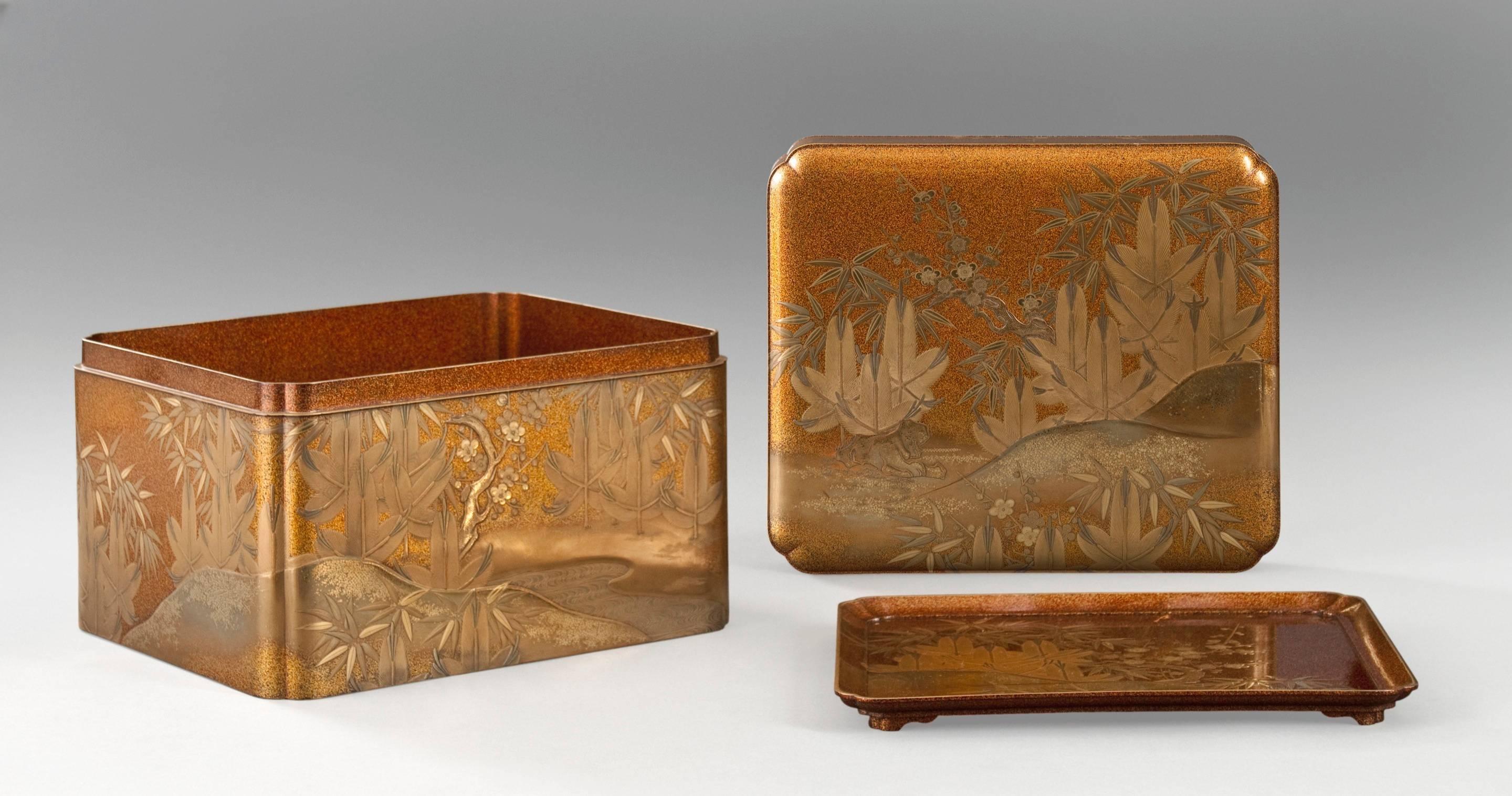 Of rectangular form with recessed corners, the top and sides depicting the three friends of winter (bamboo, pine and plum) growing amongst small rock formations, the interior tray depicting similar scenery and terminating in shaped feet, all in gold