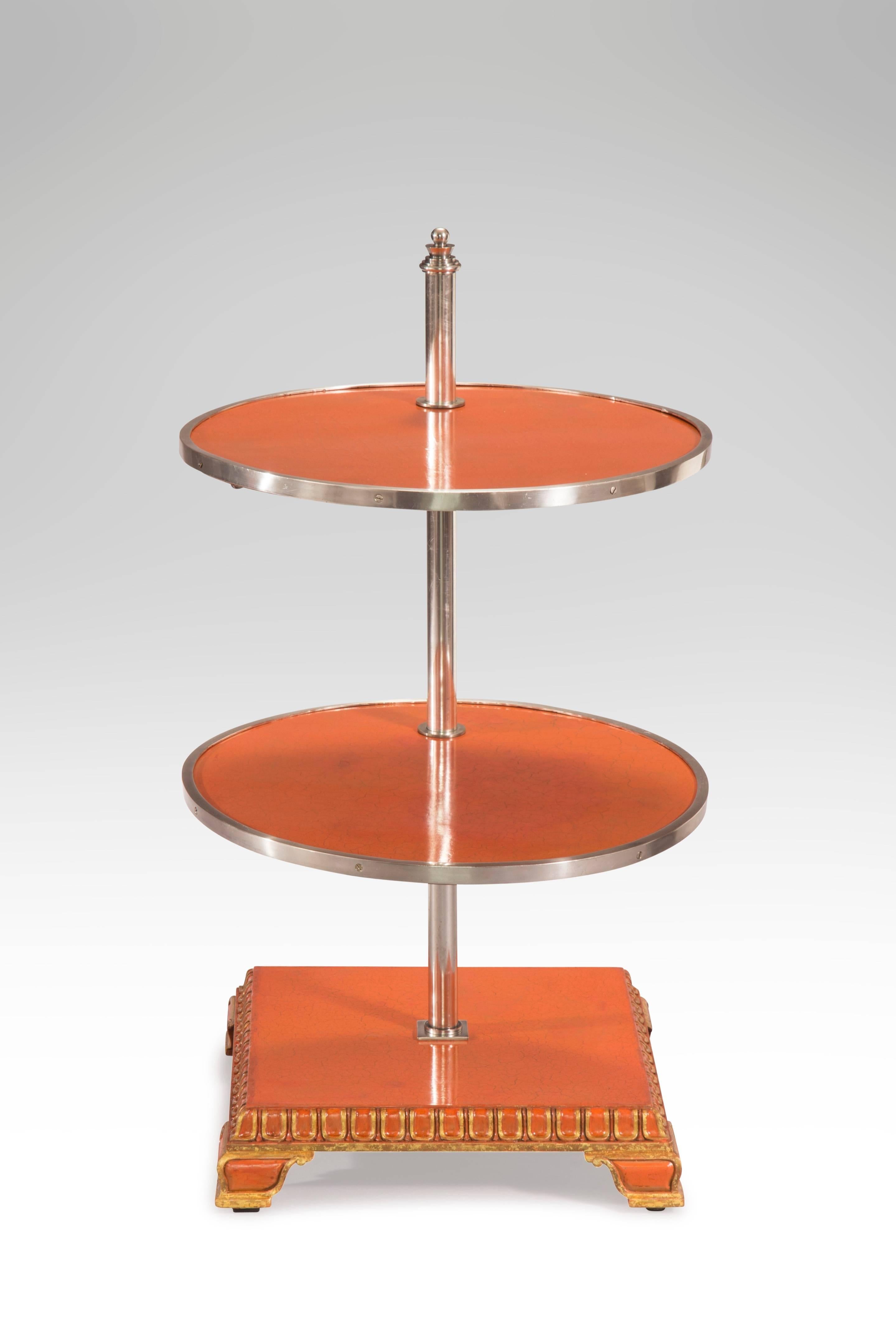 A hard to find table in very good condition with an alluring color. The metal banded adjustable round shelves, supported by a central nickel cylinder surmounted by a stylized finial, above a square pedestal base with tongue and dart molding, on