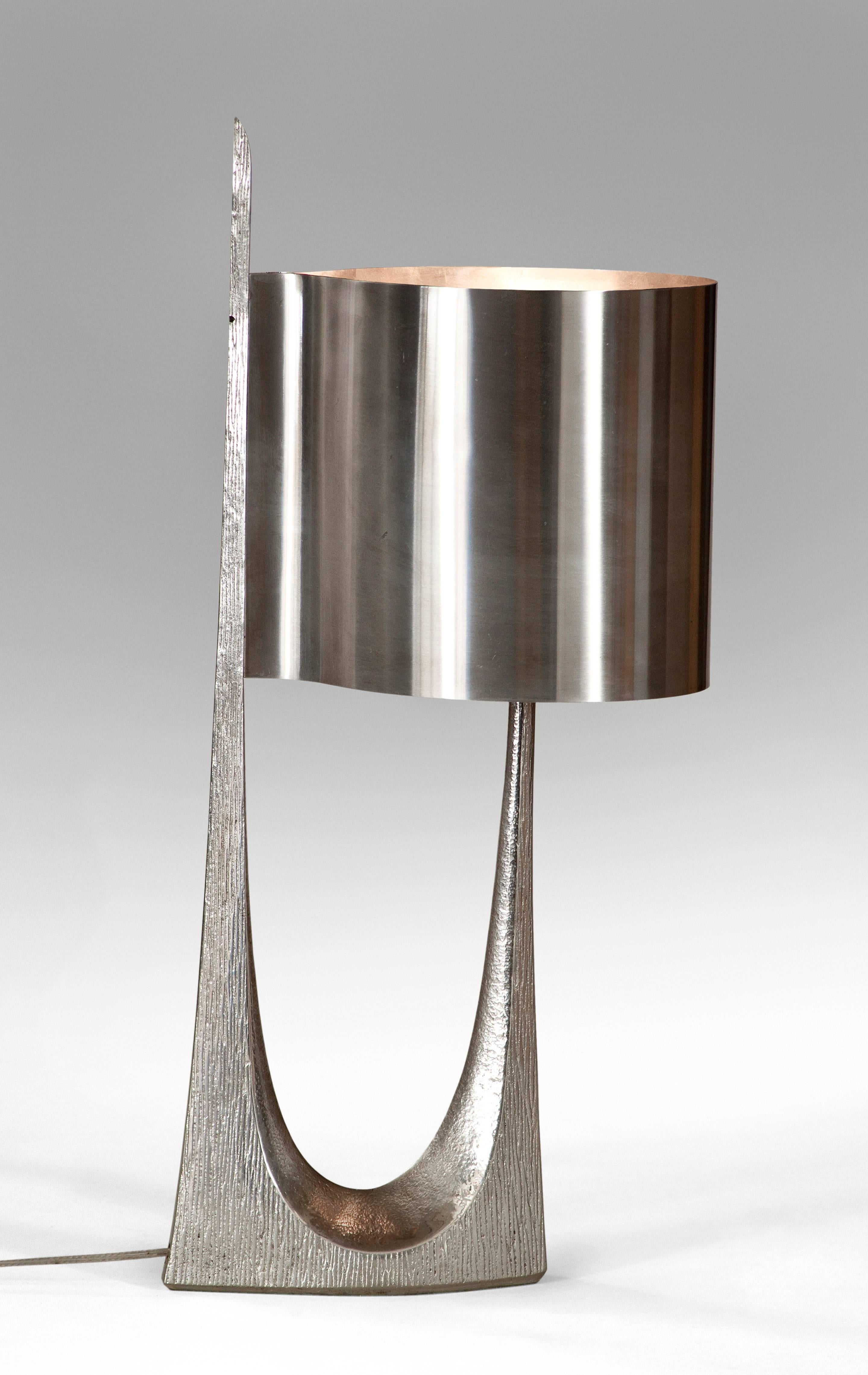 The subtle contrast between the etched surface of the heavily cast base and the polished shade are indicative of the high quality of these lamps. The textured sculptural base, holding a circular metal shade. 

The same model lamp is referenced in