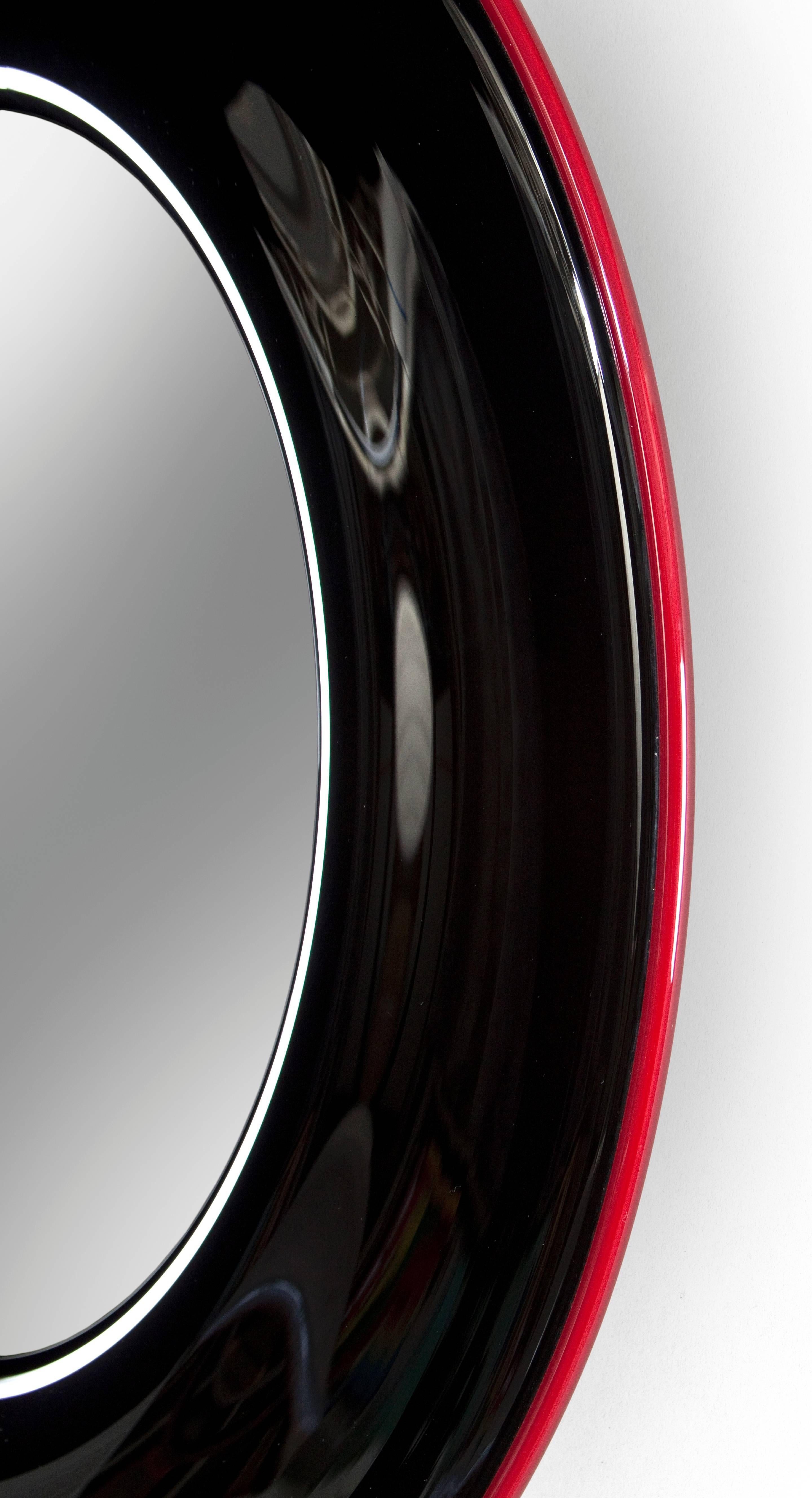 Densely colored and animated by flowing patterns of light. The circular mirror plate, within a substantial black glass frame bordered by a translucent ruby band and the frame standing proud from wall. Excellent condition.