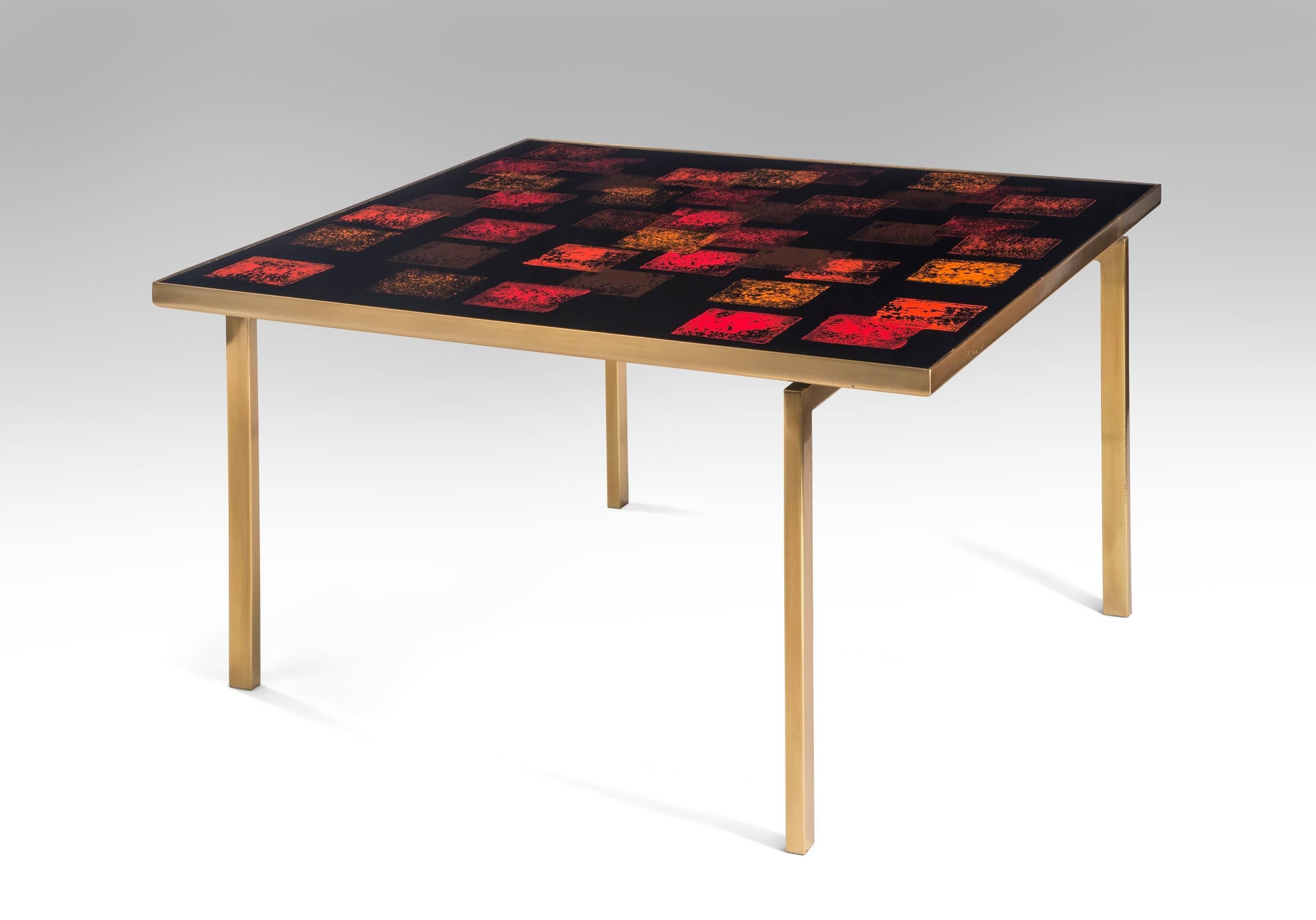 The boldly patterned iconic top floating on a sophisticated asymmetrical yet strictly geometric base. The brass banded square top composed of square patterns of varied reds and oranges over a dark background, raised on four recessed brass legs.