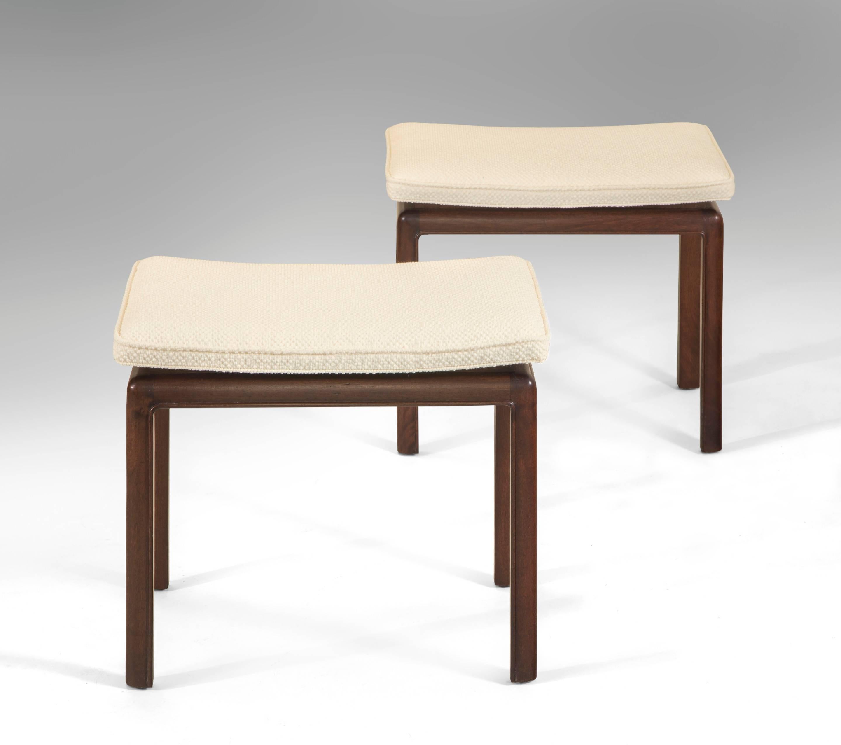 A handsome pair of elegant stools finely made. The rectangular concave upholstered seat floating above the recessed mahogany base with rounded corners and a sophisticated molded edge.