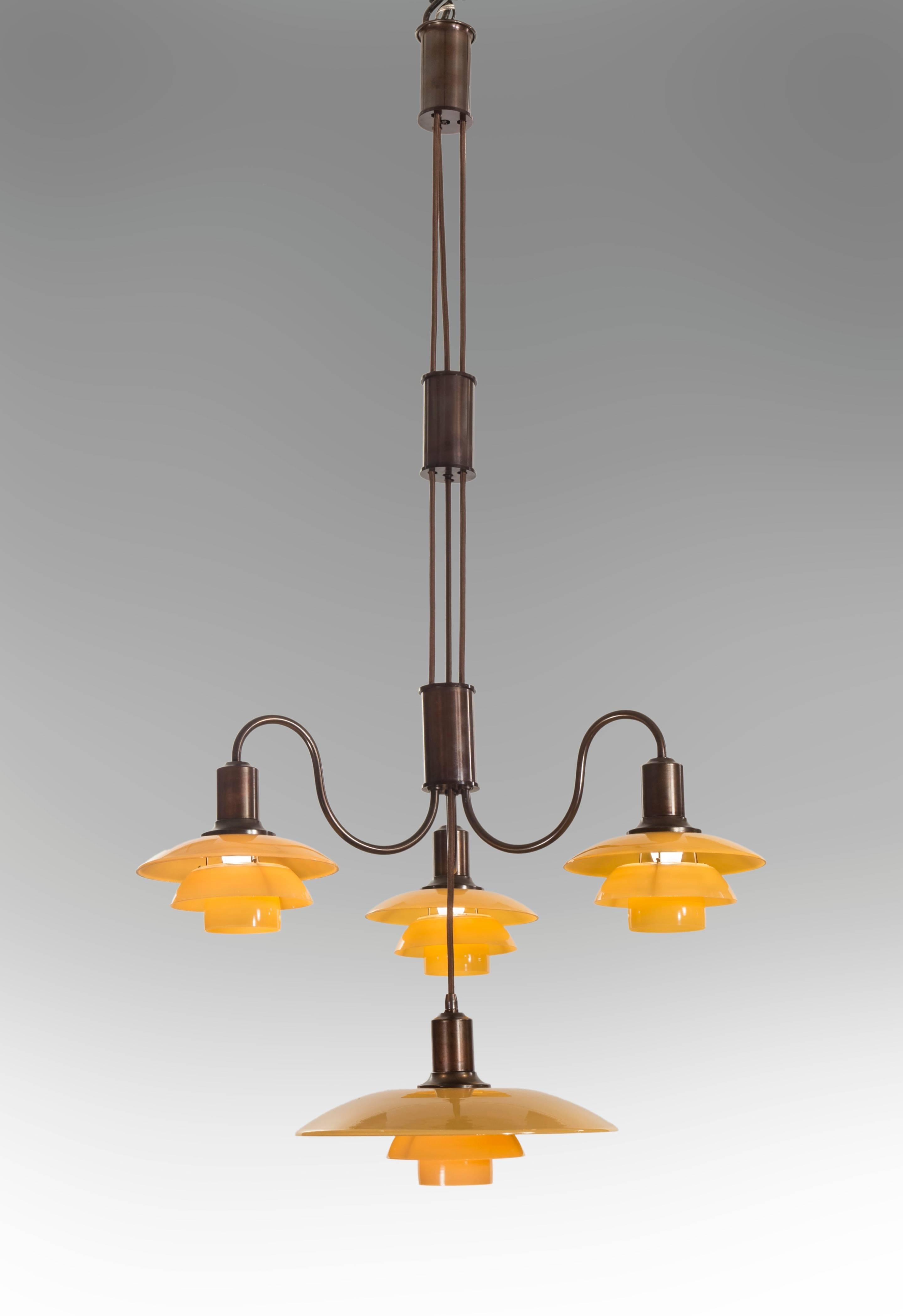 The cylindrical canopy, suspending two height-adjusting cylinders of patinated bronze connected by cords, the bottom cylinder issuing three graceful s-curved arms, each arm with a 2/2 yellow painted glass shade set, centering a 3.5/2 yellow painted