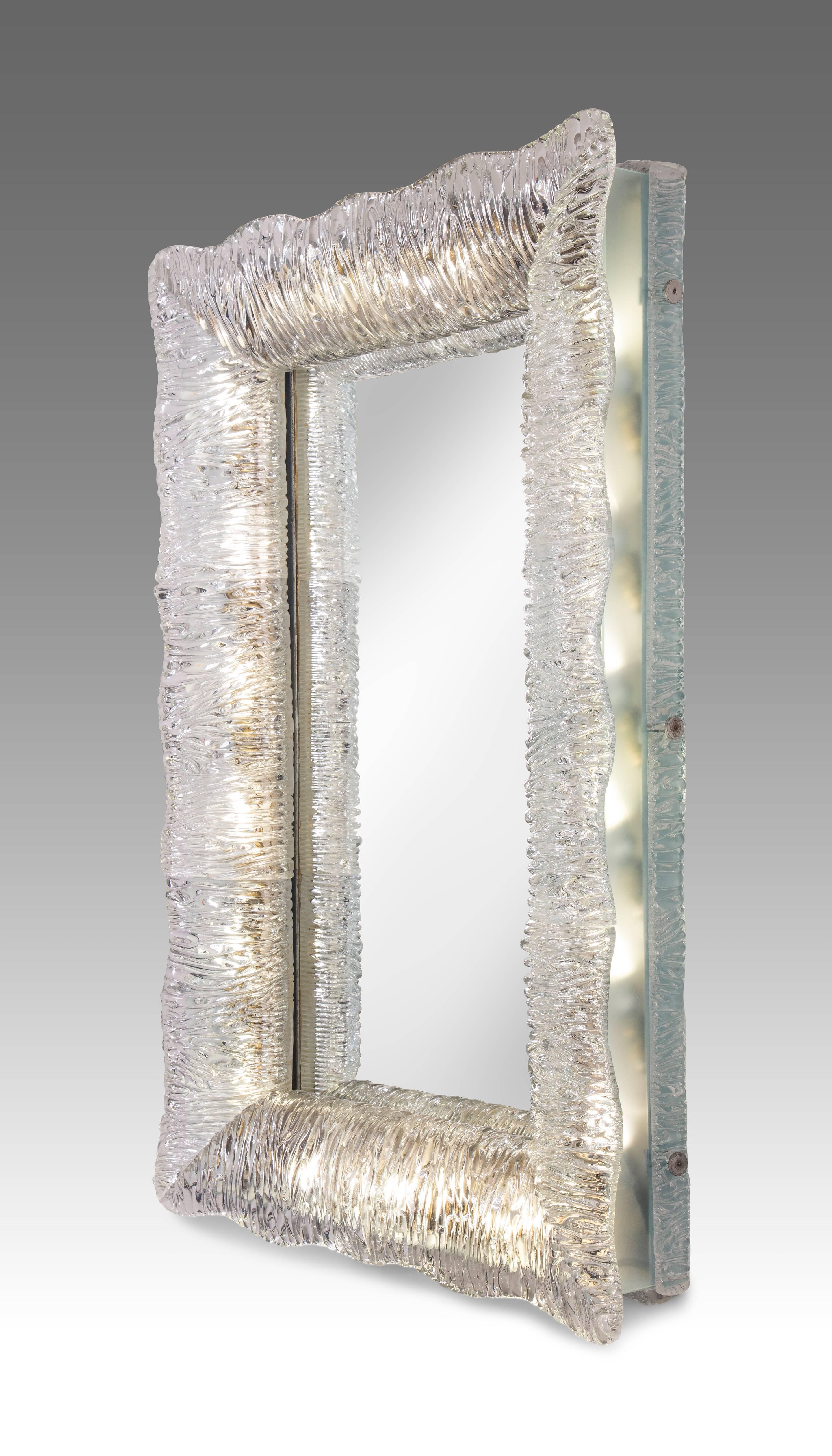 A magnificent rare example of a Venini illuminated glass framed mirror. The rectangular mirror plate within a frame composed of textured glass with undulating edges, softly illuminated by lights concealed by frosted glass side panels. Original