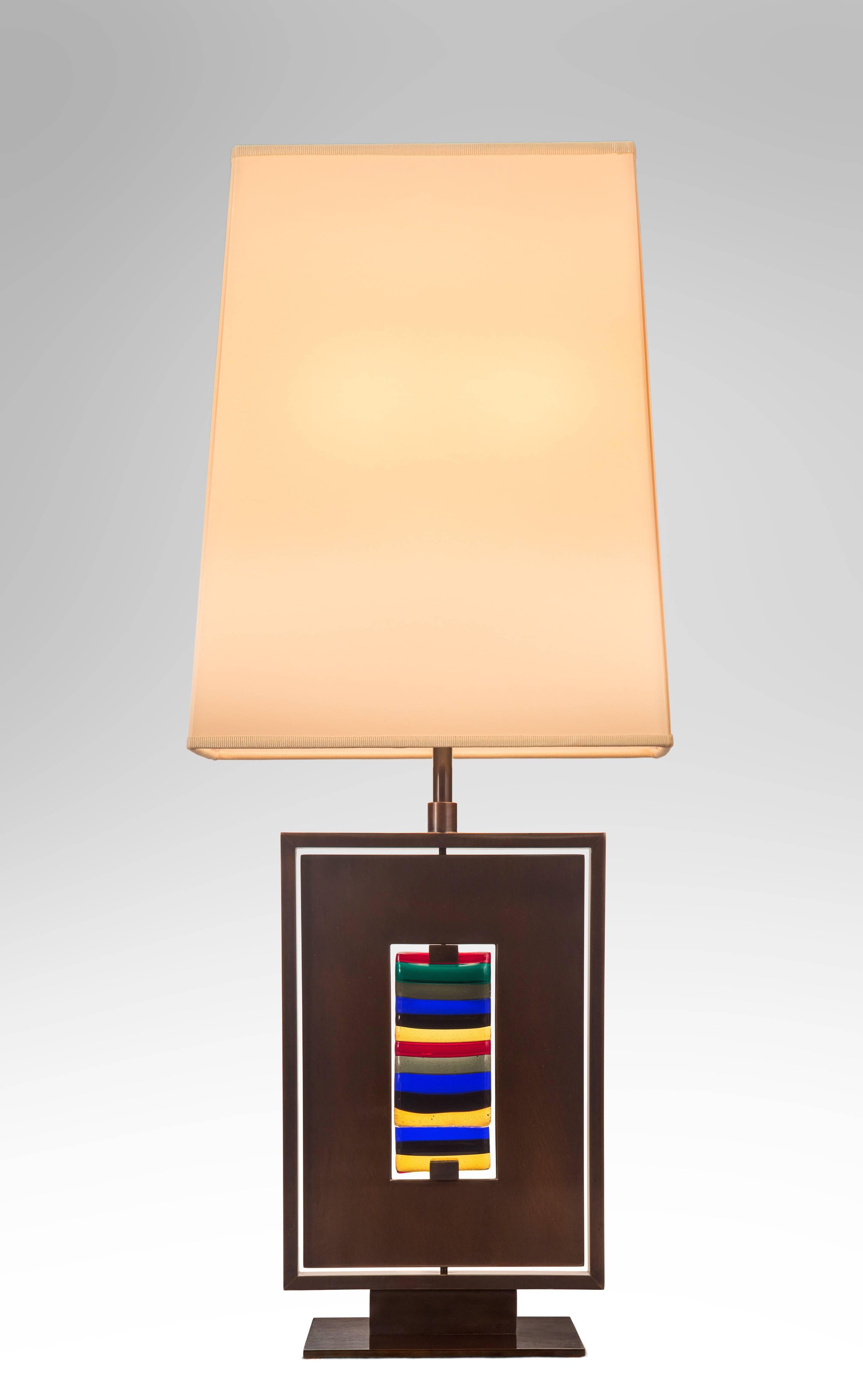 Each with a tapering silk shades above a rectangular gunmetal patinated frame centering two separately rotating panels, one metal and the other a multicolored Venini glass panel, raised on a pedestal with a rectangular base.