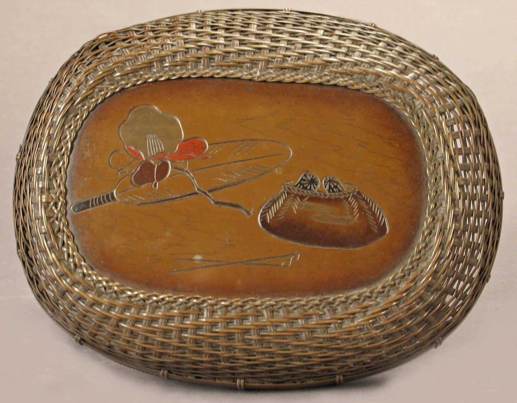 Amazing! An ingeniously woven metal basket. The whole of various woven patterns in brown and black, the lid and base divided by two brass bands, the top with an oval engraved panel, and fitted with two swing handles.