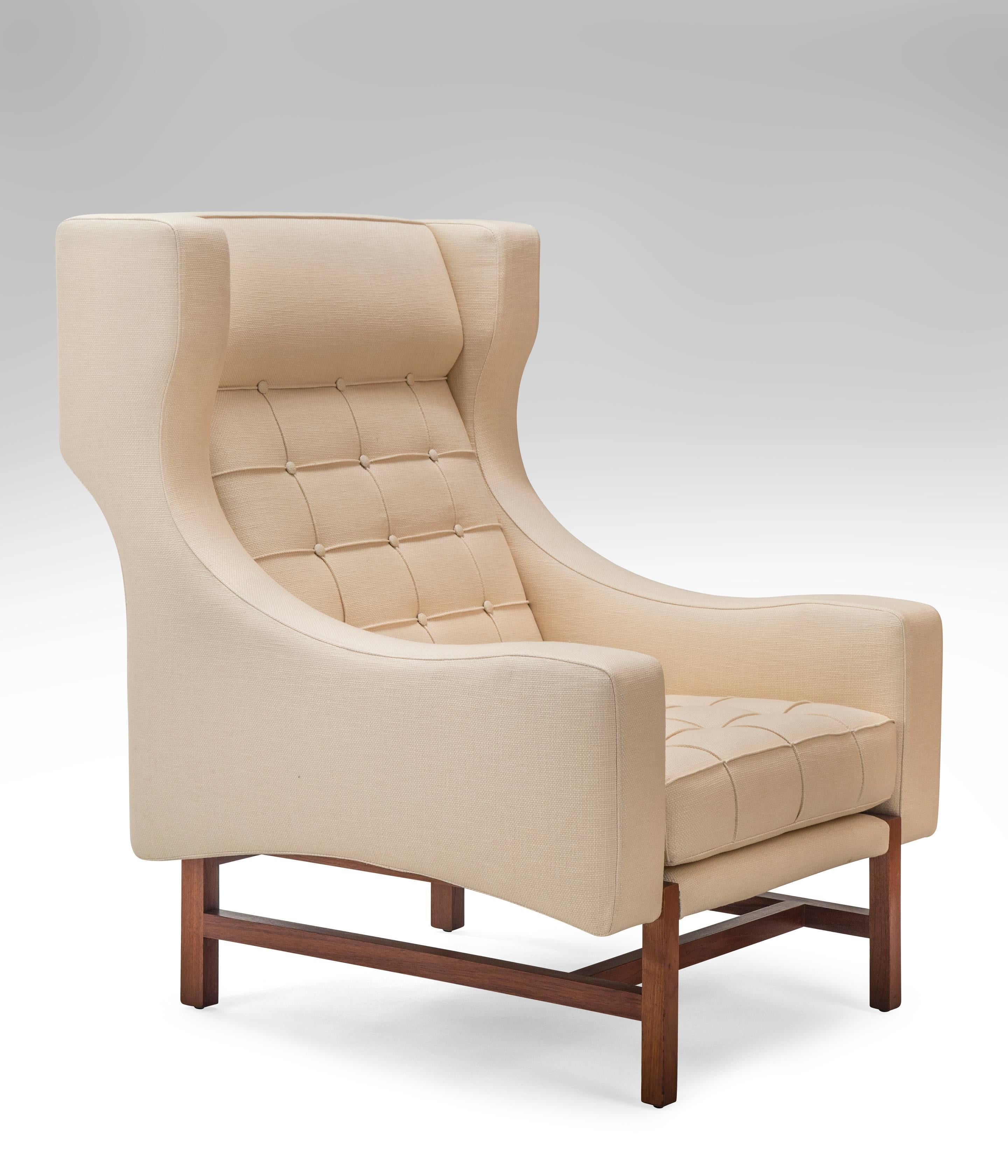 Very rare stylish wingback chairs and ottomans, large scale and comfortable. The inventive updated wingback above a square seat flanked by shaped arms, resting on walnut legs joined by stretchers, the seat and back fabric stitched with