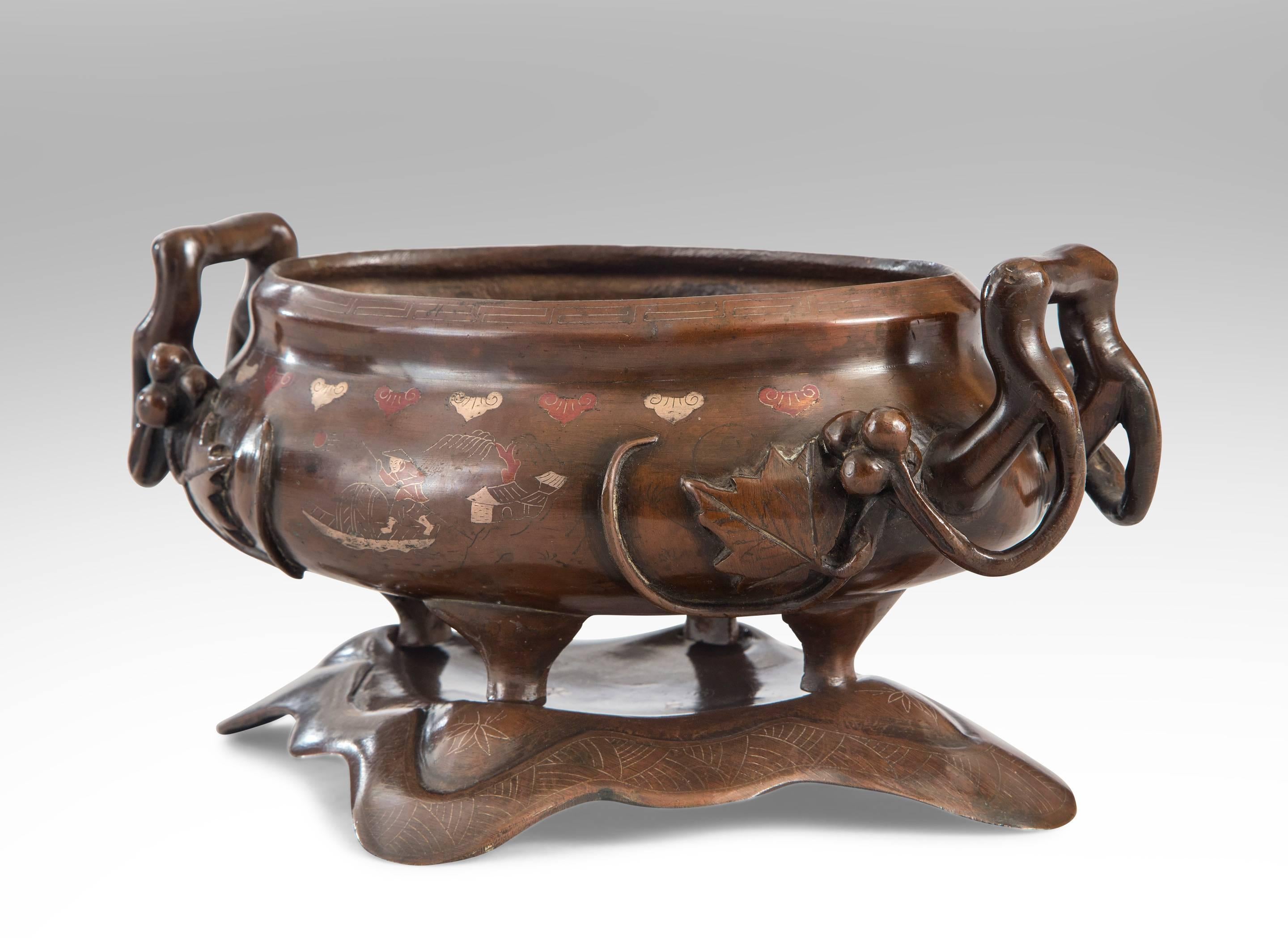 Of such fine quality even the unseen base is decorated with a inlaid trailing flowers. The oval bowl with an inlaid silver Greek key border and polychrome scenes of fishing and agriculture, the berry and foliate relief handles, on four legs set into