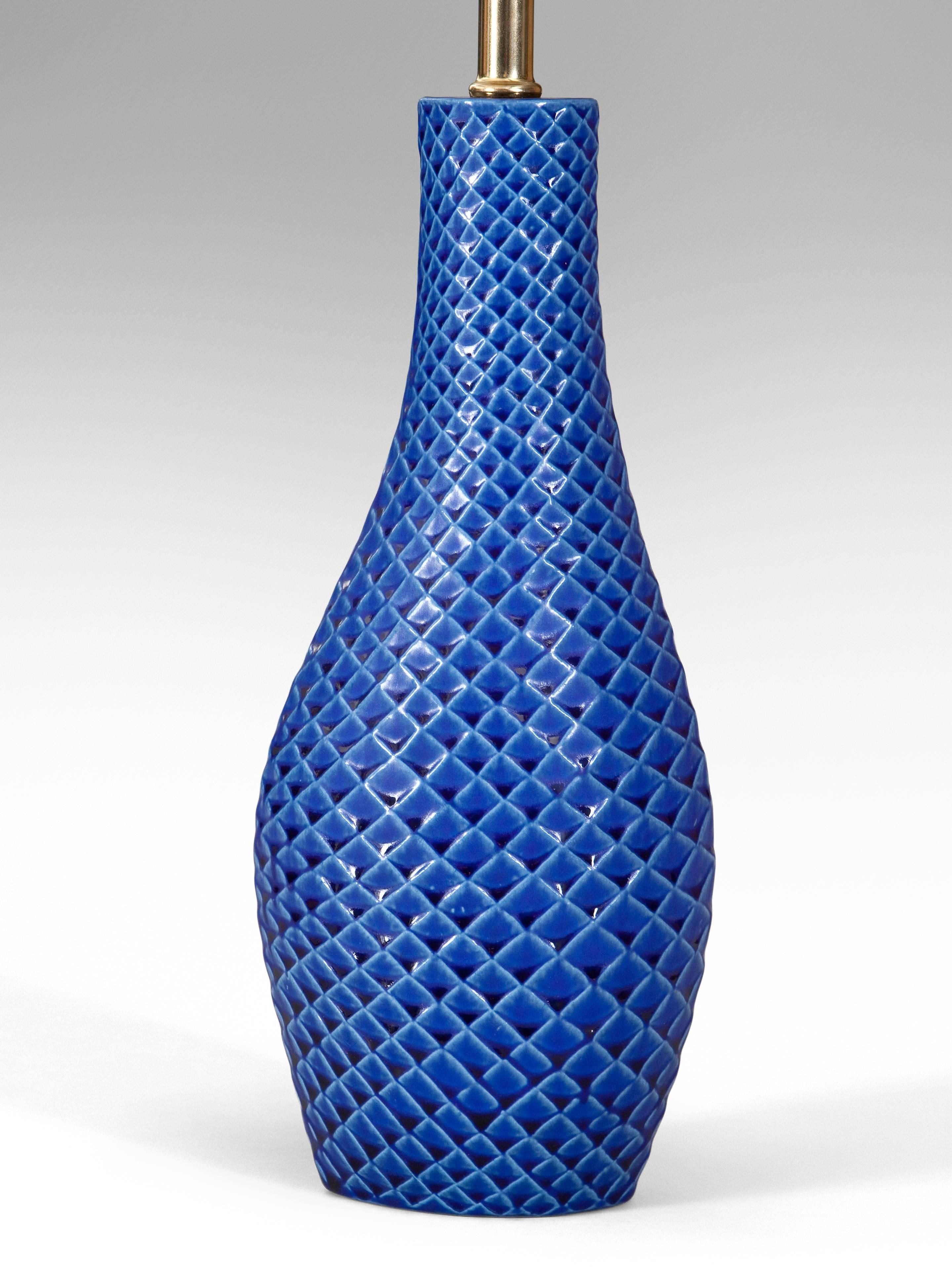 Each lamp with an elliptical mouth above a conforming neck and slightly asymmetrical swollen base, adorned in parallel scoring creating a scale-like pattern. A wonderful intense blue glaze.