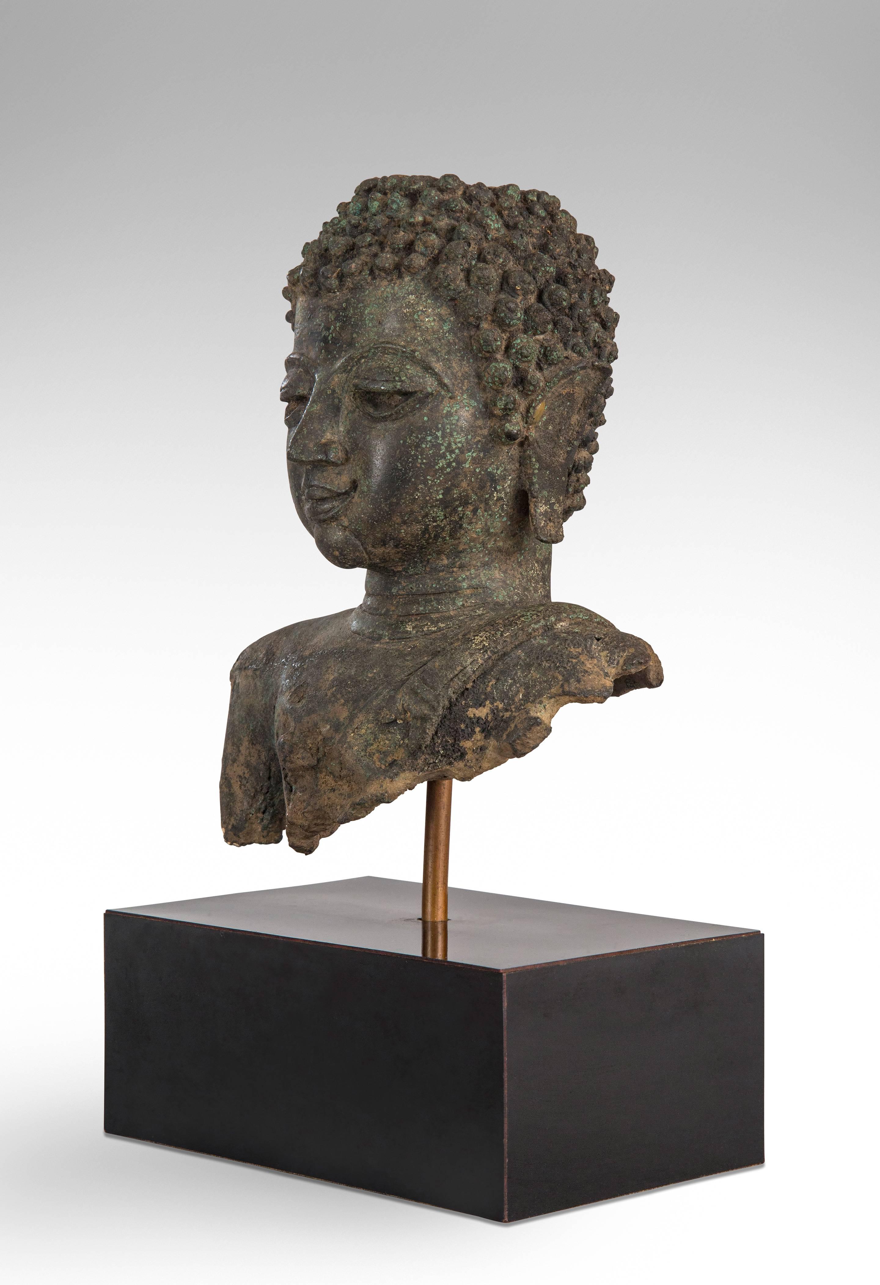 Chiang Saen period Thai patinated bronze Buddha head 
With a sash draped over his shoulder, the face displaying a calm expression with high-arched eyes, elongated earlobes and Ketumala missing.
circa 1380.