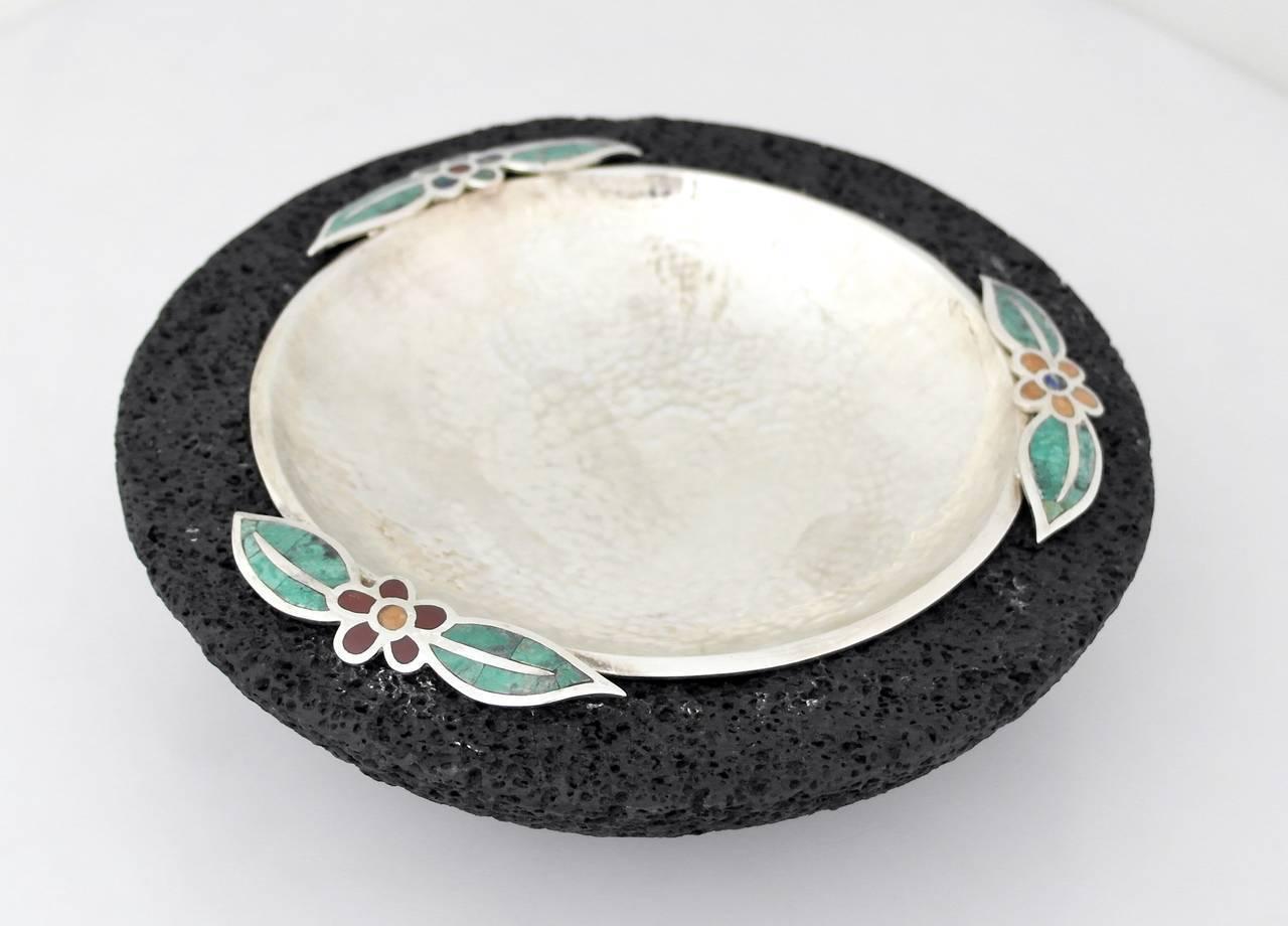 Being offered is a circa 1990 serving bowl by Emilia Castillo of Taxco, Mexico. Hammered bowl with three floral motifs, placed in a lava rock formed bowl. Silver bowl is removable for cleaning. Dimensions: 10 inches diameter. Marked as illustrated.