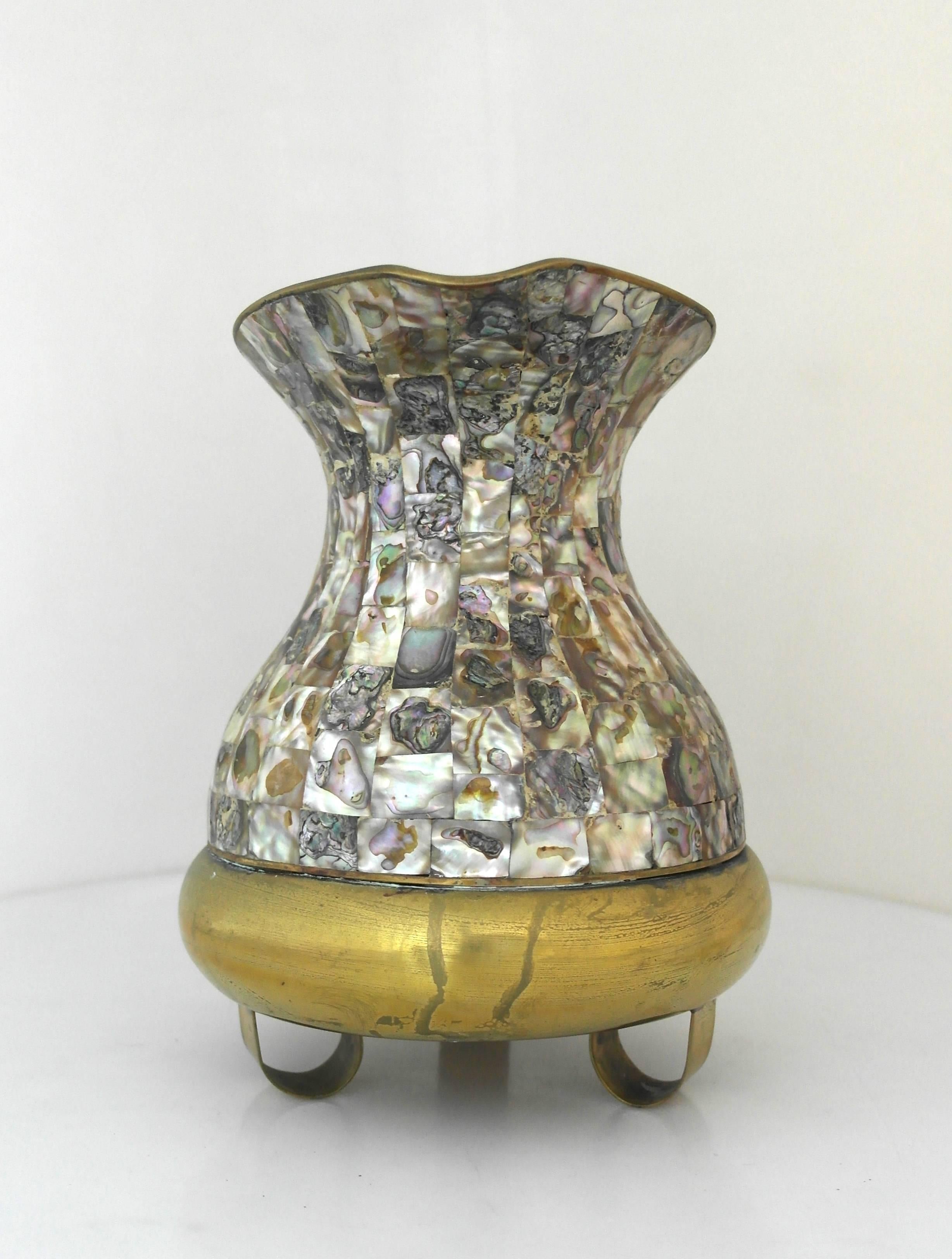 Being offered is a circa 1950 brass pitcher made in Mexico. Handmade brass object with panels of abalone inlay on the body and handle; resting on three curved feet. Dimensions: 9 1/4" tall x 6 1/4" diameter x 9" from handle to spout.