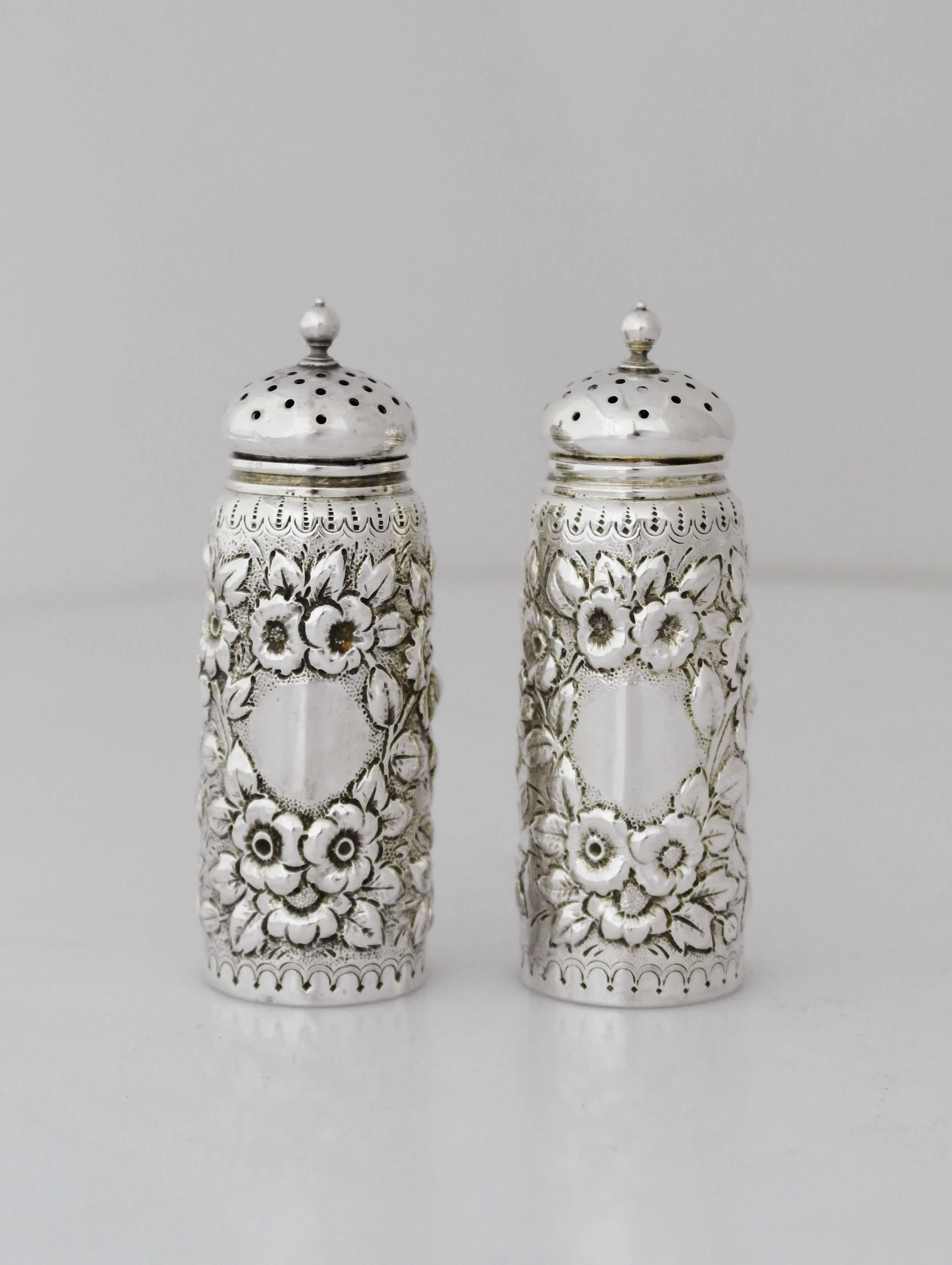 Being offered are an incredible pair of sterling silver salt and pepper shakers by Dominick & Haff of New York, New York. Tall, cylindrical form shakers with hand decorated floral motifs throughout, domed, pierced lids with ball finials. Dimensions