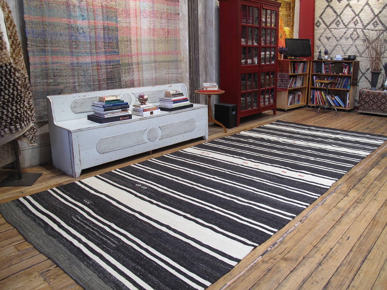 An old Kilim from Central Turkey in the characteristic wide runner format, woven with wool and goat hair in alternating dark brown (almost black) and off-white bands. A scattering of brocaded 