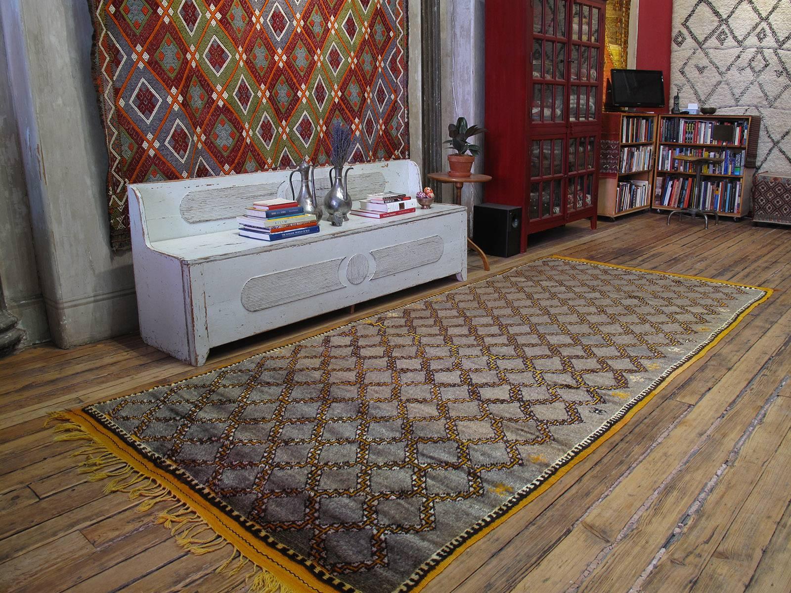 A beautiful old Moroccan carpet from the High Atlas Mountains, woven in wide runner format, with a finer weave and a more precise drawing than is usual in Berber weaving tradition. The background is natural wool in gray-brown and the small scale