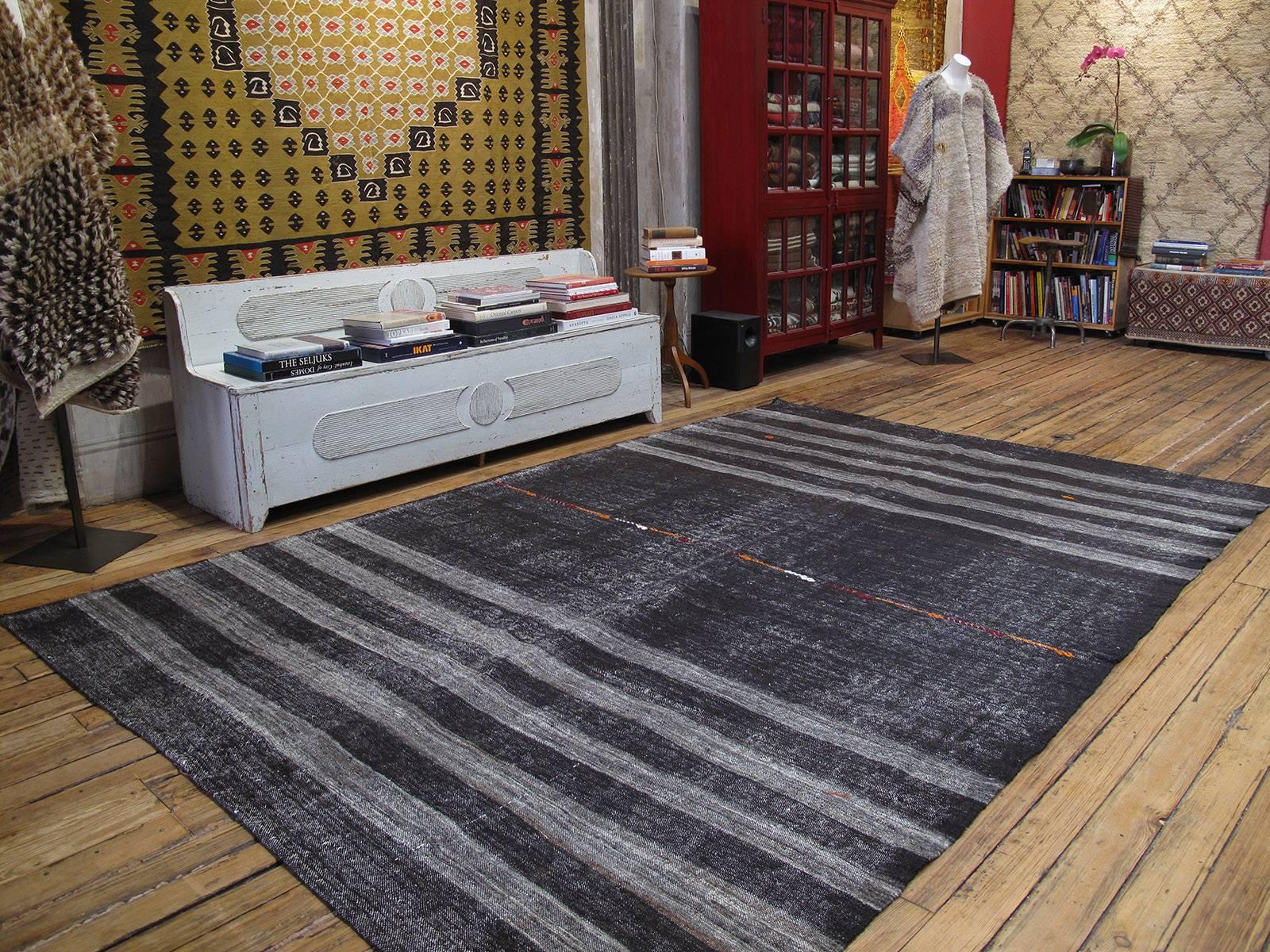A large, primitive, dramatic tribal flat-weave woven entirely with goat hair in natural dark brown (almost black) and gray bands. Woven as a utilitarian floor cover, it has a rough texture. A line of colorful motifs in the center, woven in brocade,