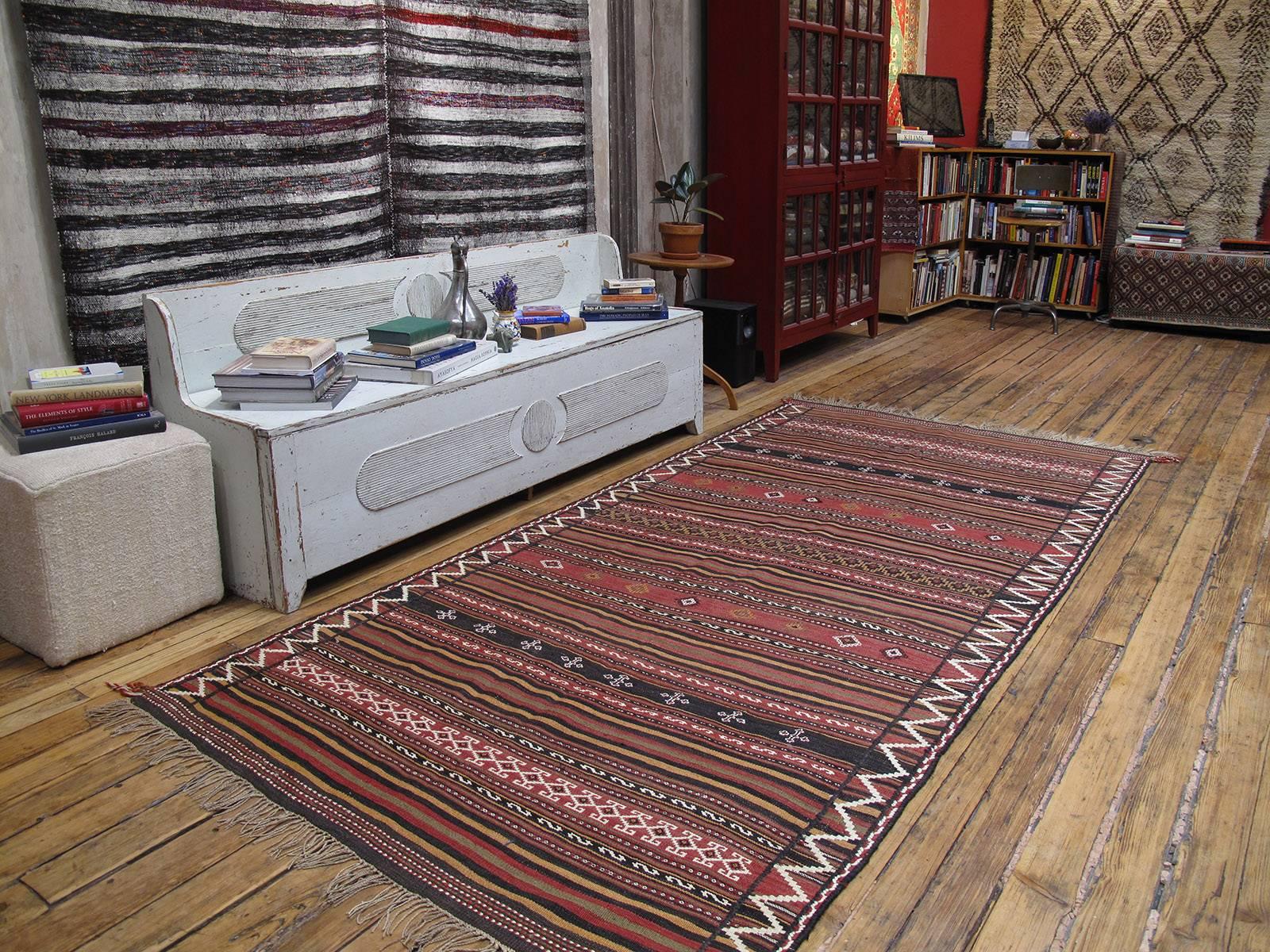 A tribal kilim by the Baluch weavers in their traditional design, color palette and technique: bands decorated in various brocading techniques alternating with plain multi-colored stripes, with a striking zigzag border in white wool. Very well