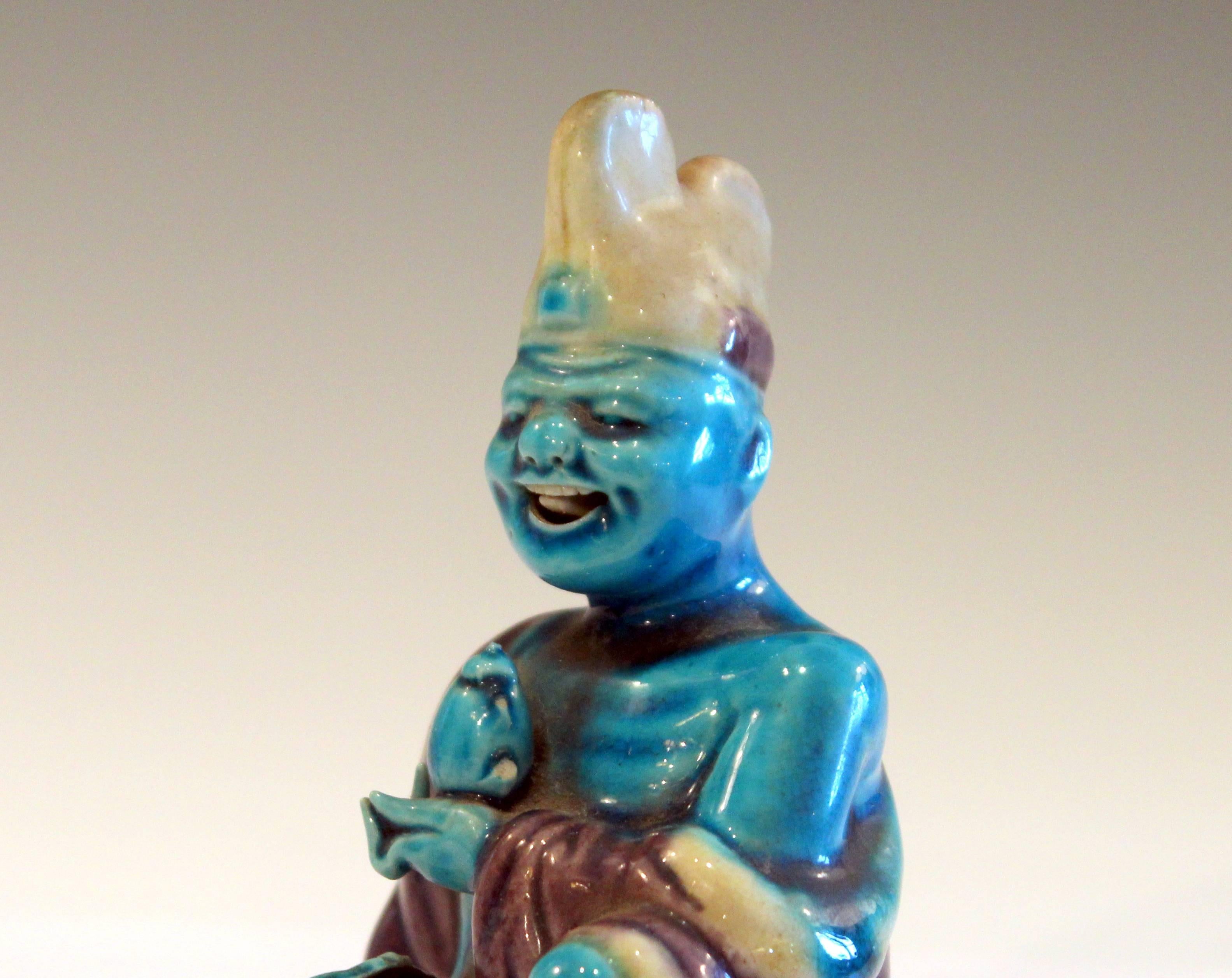 Chinese porcelain lecherous spirit figure mischief maker with bobble tongue that wags lasciviously behind an expansive grin, circa early 20th century. Figure is holding a teapot and a palm frond and wears a large double peaked hat. Measure: 4 1/2