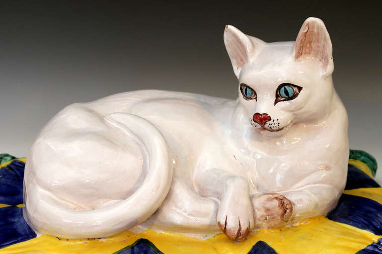 Große, gepresste italienische Terrakotta-Skulptur einer weiß getigerten Katze, die sich auf einem mit Quasten verzierten Kissen mit lebhaftem blauen und gelben Rautenmuster räkelt, um 1960er Jahre. Realistisch modelliert und mit markanten blauen